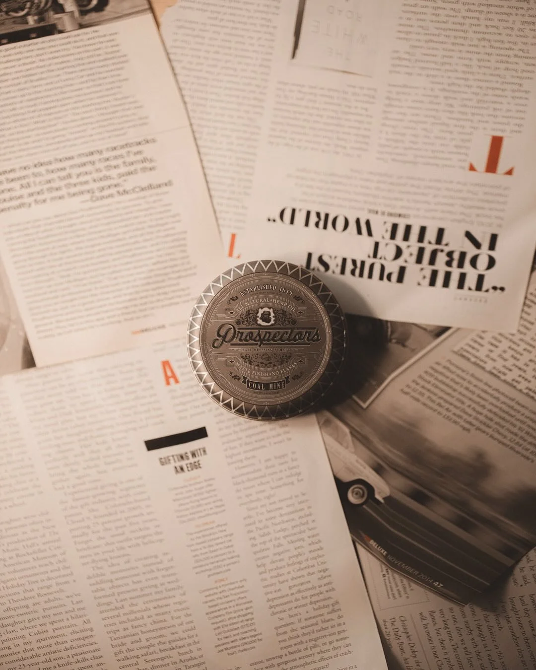 A tin container of Prospector hemp oil placed on top of scattered newspaper pages.