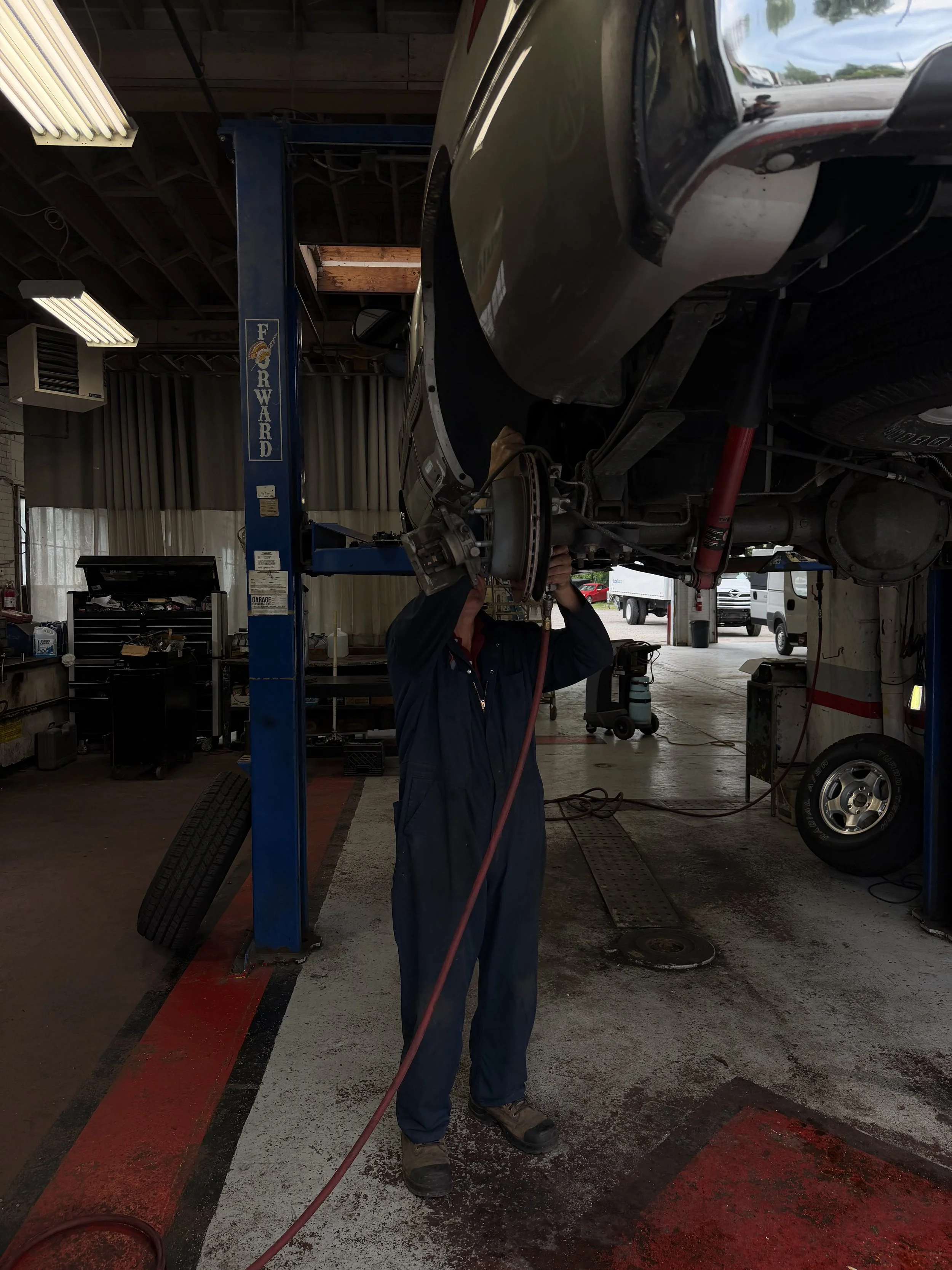 A mechanic working underneath a vehicle on a lift at an auto repair shop.