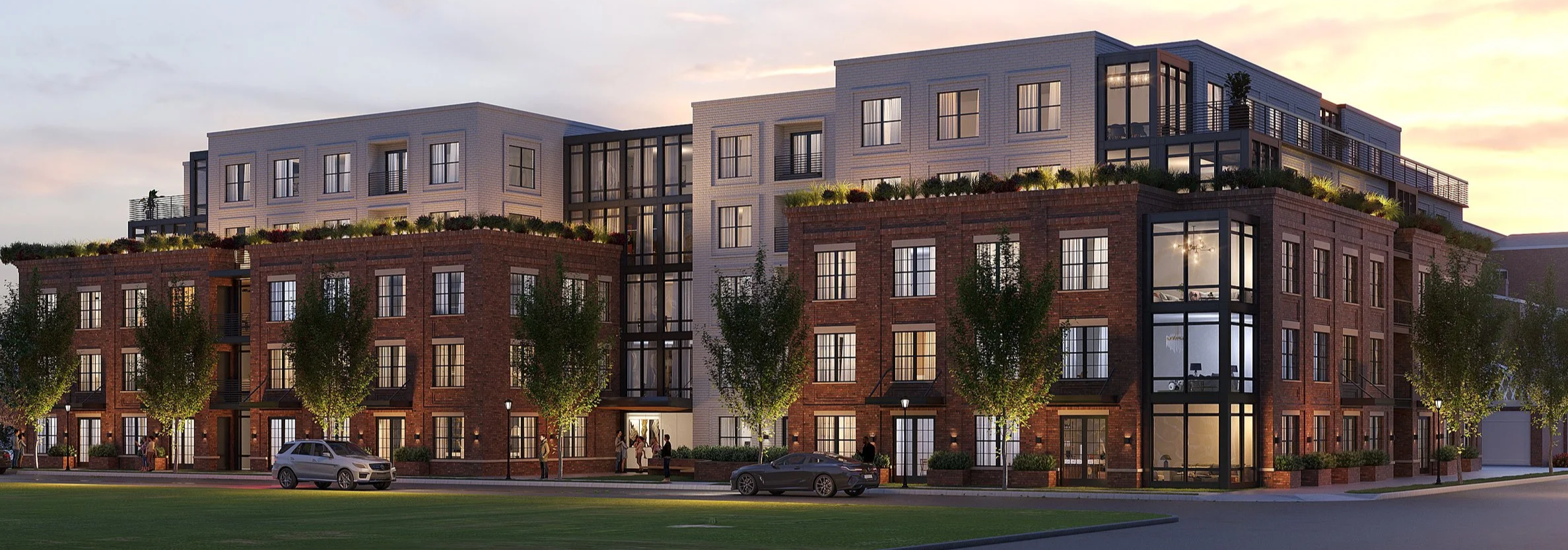 Modern multi-story apartment building with brick and white exterior, large windows, and balconies, surrounded by trees and parked cars at dusk.