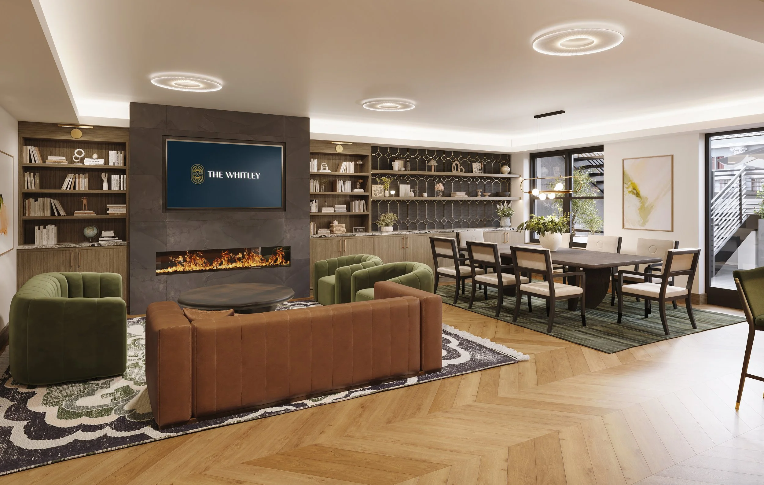 A modern living and dining room with a fireplace, a large television screen with 'The Whitley' logo, bookshelves, a glass dining table with chairs, and large windows with a staircase outside.