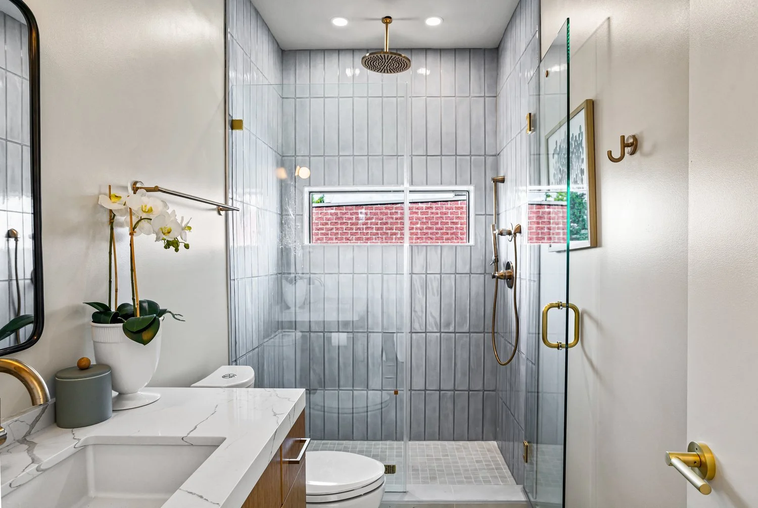 Modern bathroom with a glass-enclosed shower, marble countertop sink, and a potted orchid plant.