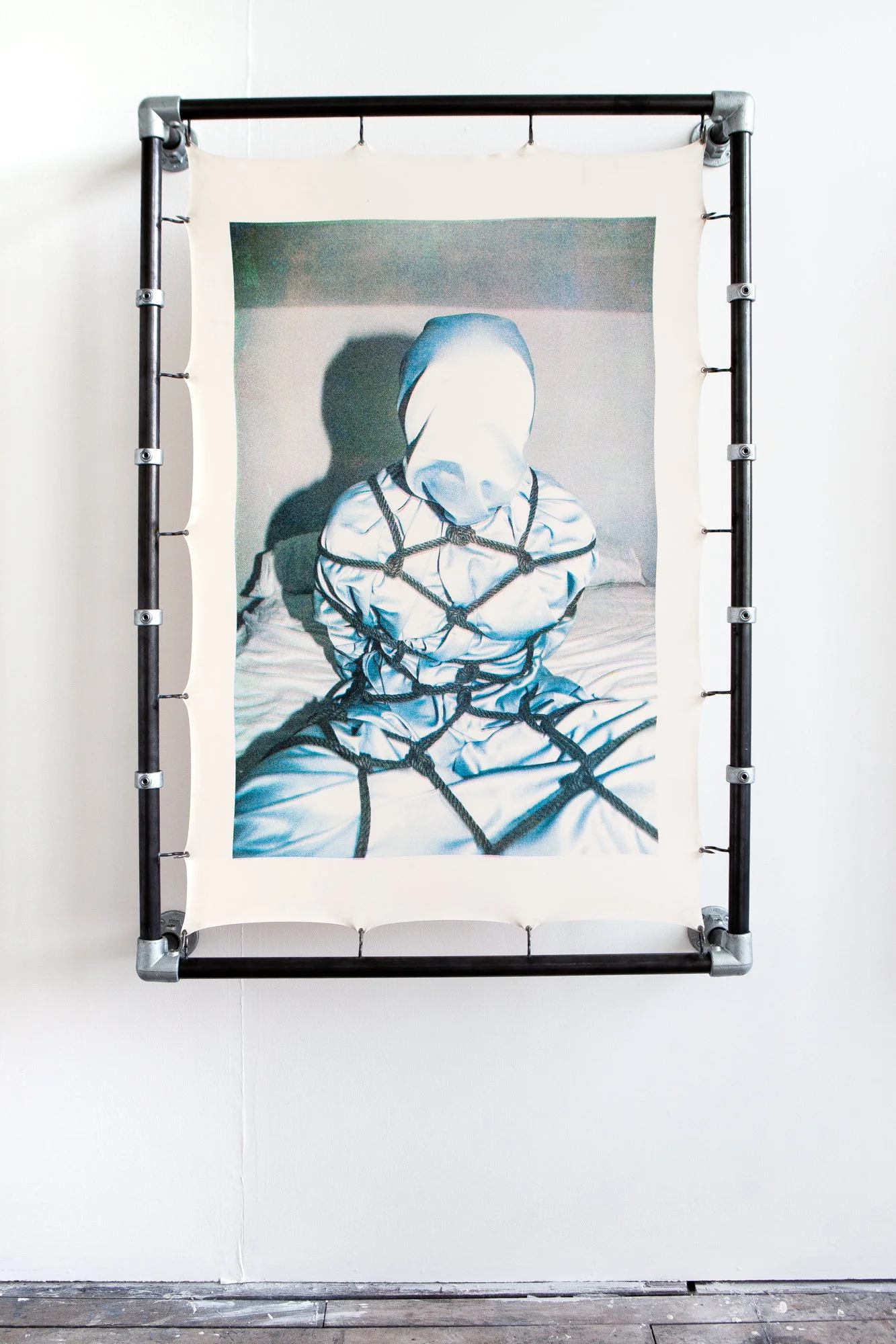 An art piece depicting a person with a cloth covering their face, seated, with a net draped over their body.