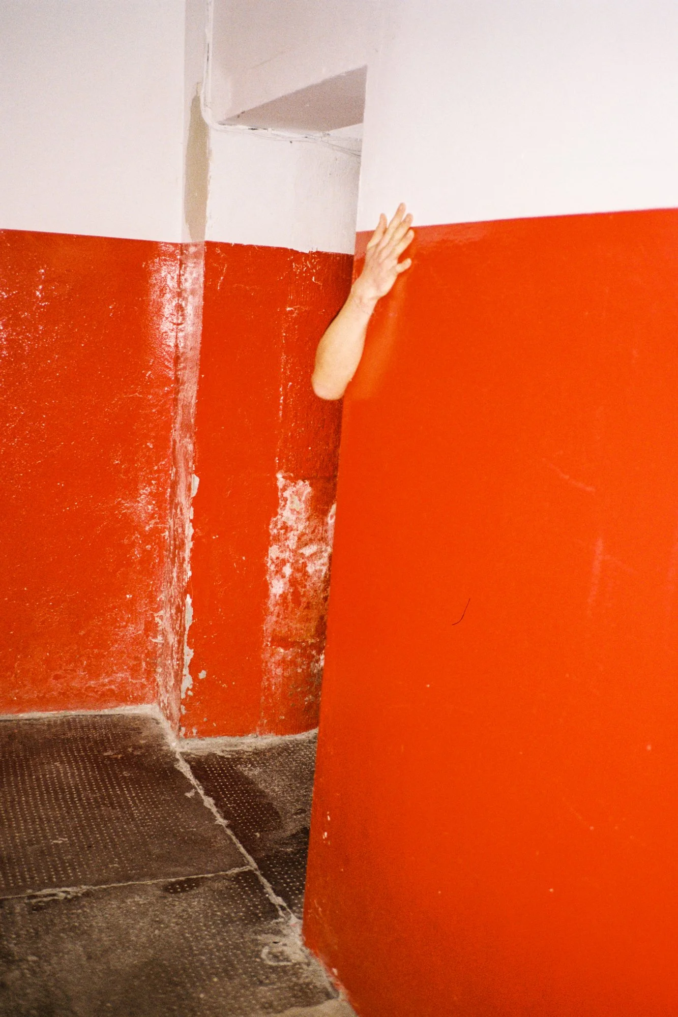 A person painting a wall with orange paint, with some area of the wall unpainted and white. The person’s hand is visible, holding a paintbrush or roller.