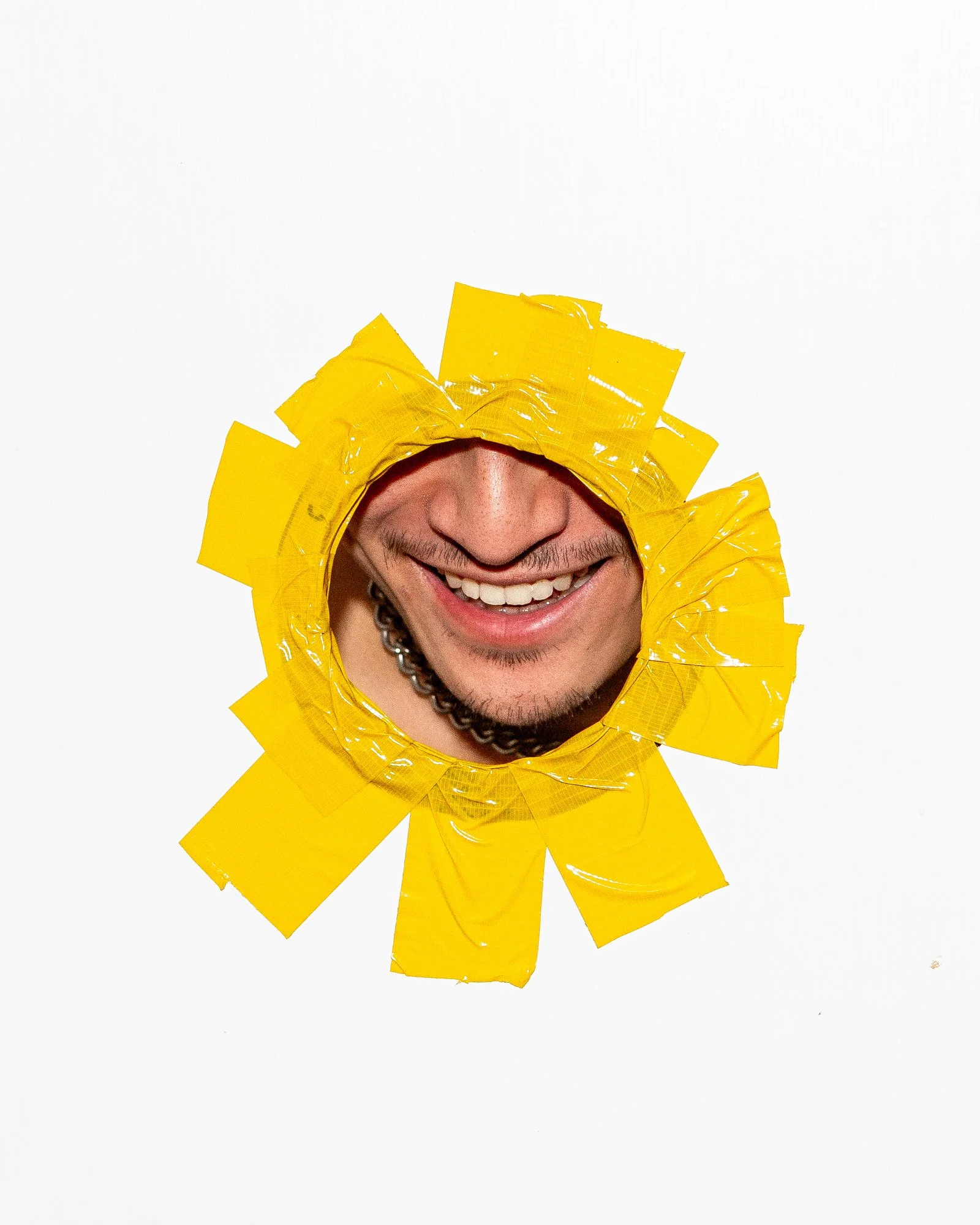 A person's face smiling through a yellow collar made of duct tape, with the top of the head and eyes covered.