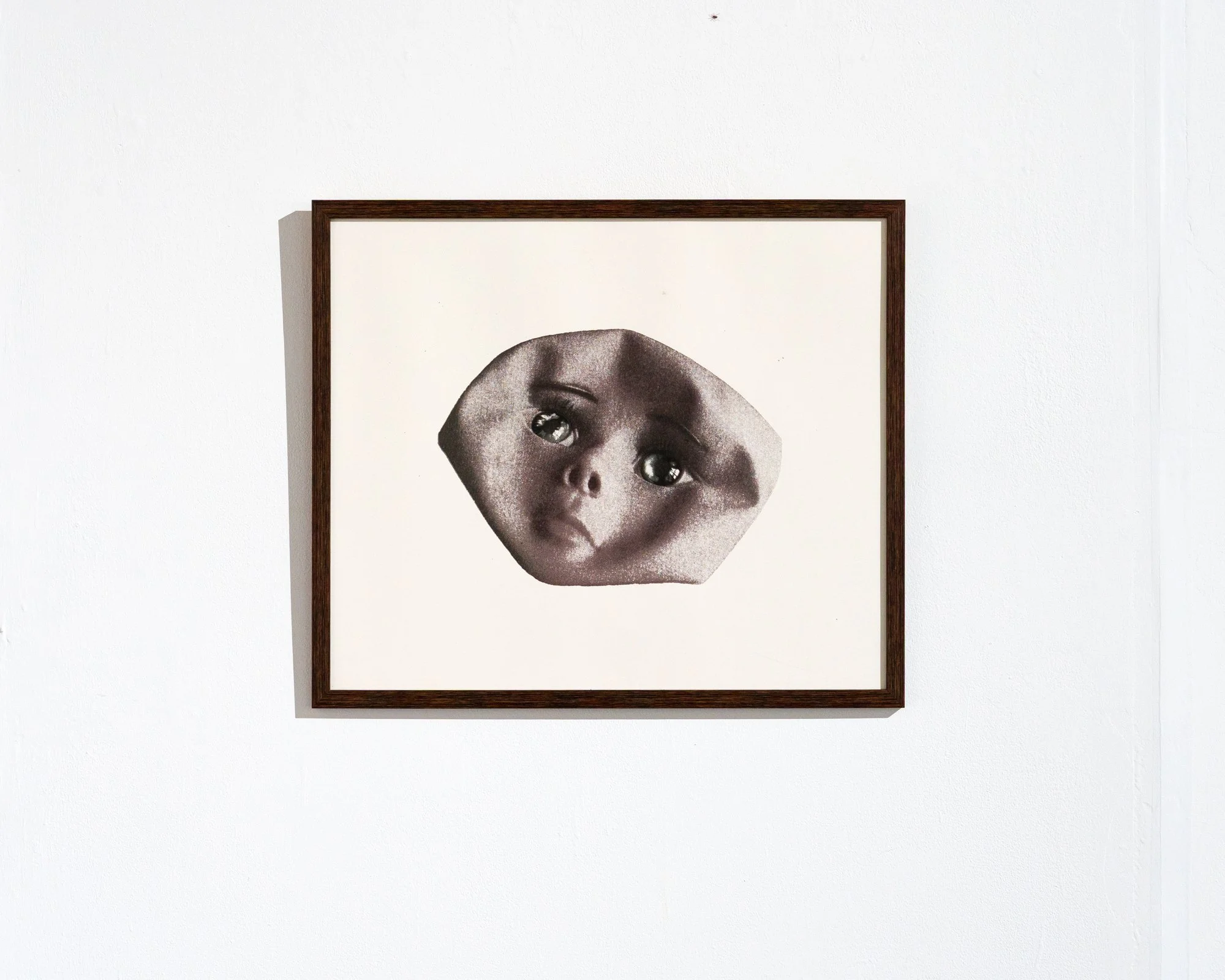 Black and white drawing of a child's face with exaggerated features, framed and hanging on a white wall.