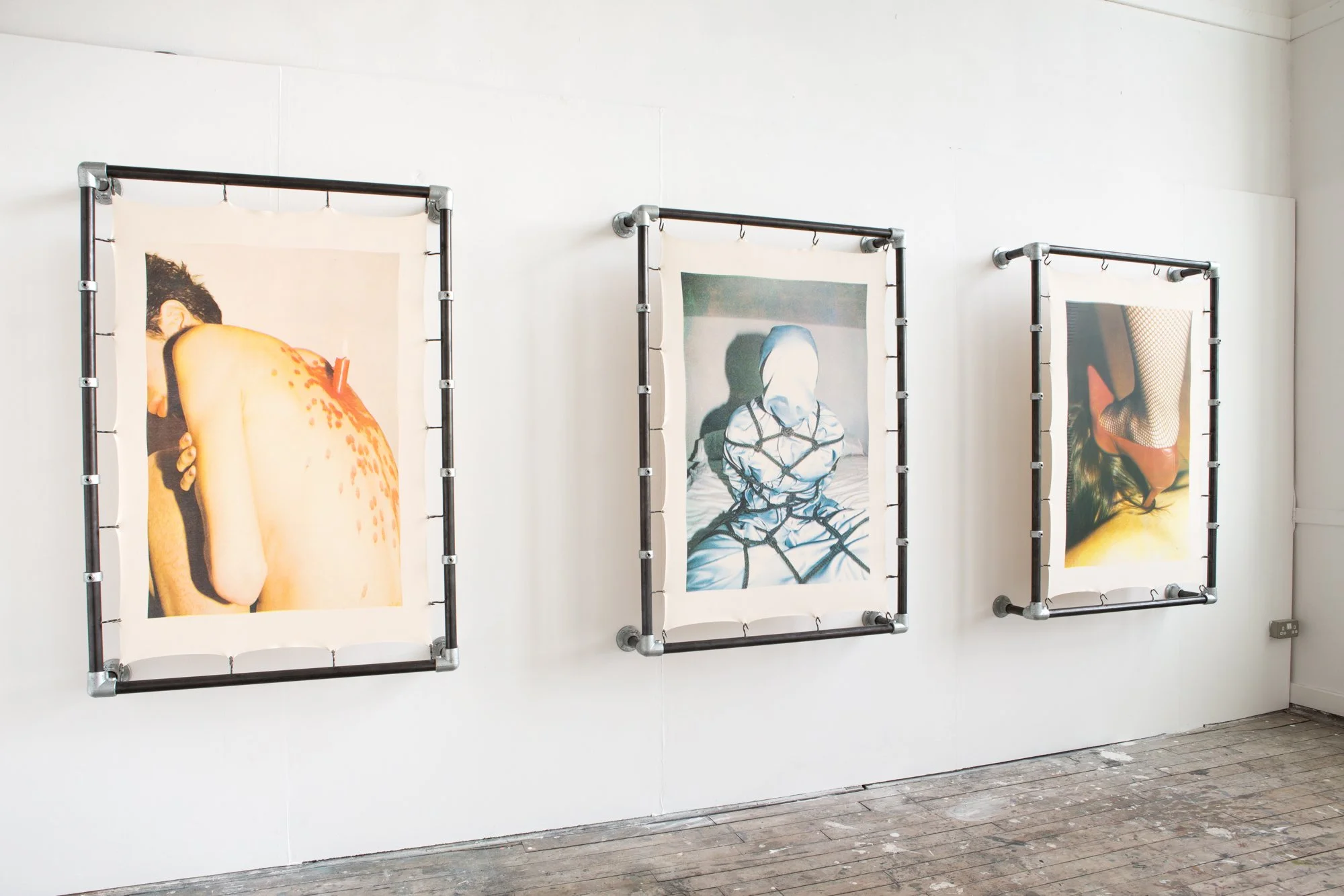 Three connected art prints on a white gallery wall, framed with black pipe, featuring abstract and distorted human figures.