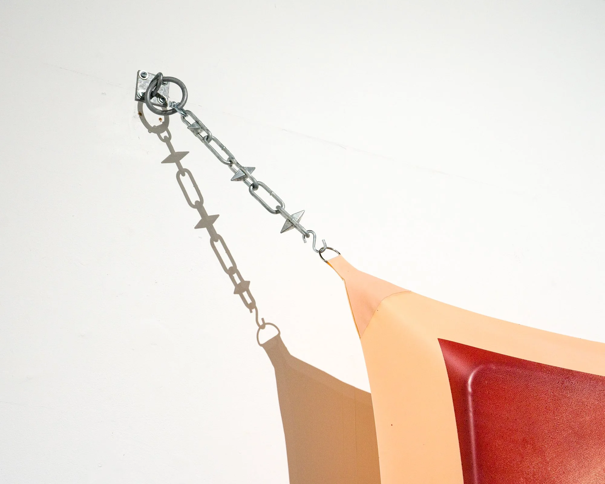 A person with a cartoon-like arm reaching toward a white wall with a small metal latch and chain attached, casting a shadow of the chain and latch on the wall.