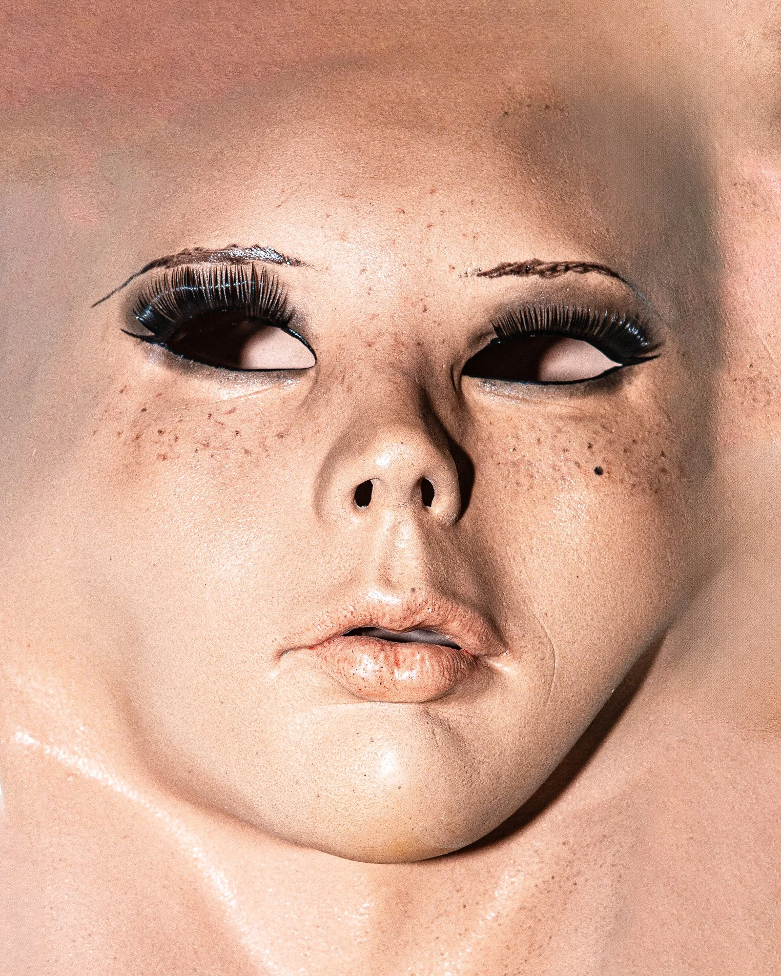 Close-up of a person's face with makeup, including bold eye makeup with long eyelashes, brown eyes, and neutral lips.