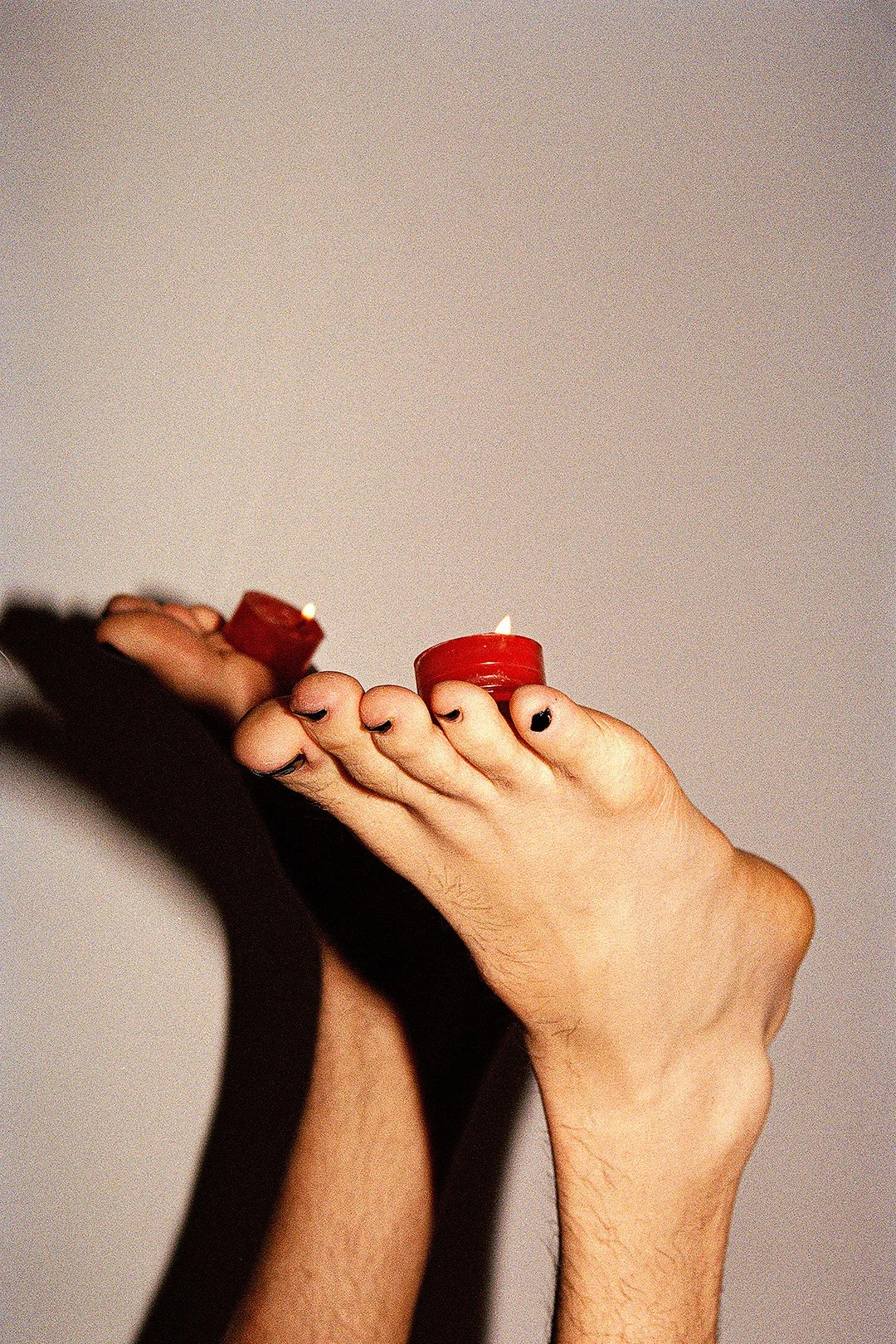 Two hands holding small red candles, casting shadows on a plain background.