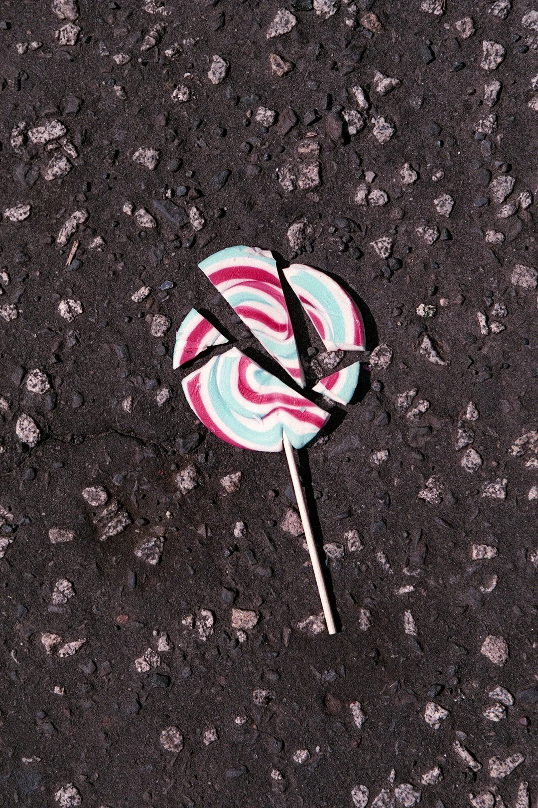 Broken colorful swirled lollipop on asphalt ground.