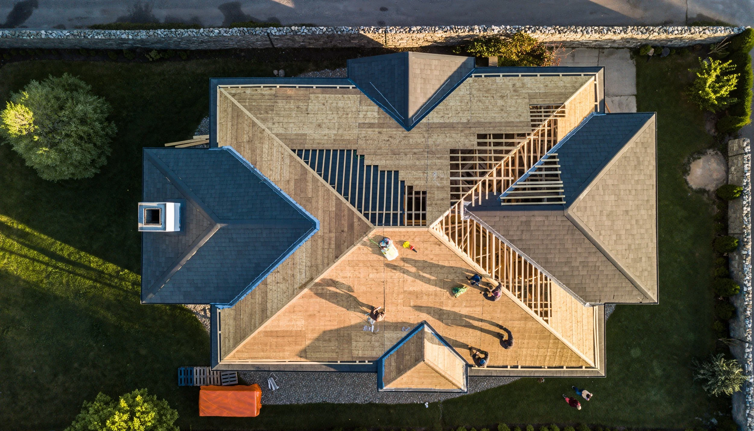 An aerial view of a house under construction with framing and roof partially completed, and people on the roof working on the project.