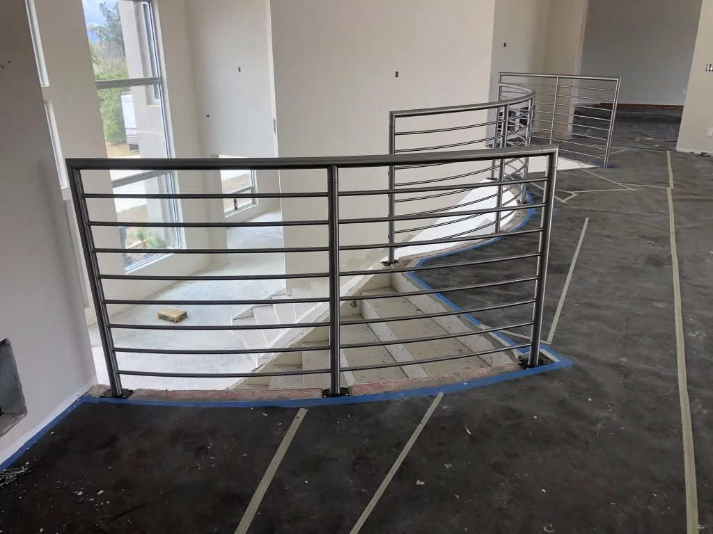 Interior view of a house under construction with a metal railing around the staircase opening, unfinished flooring, and taped areas.