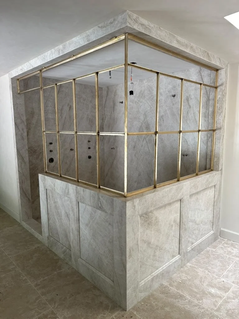 Construction in progress of a kitchen island with a wooden frame, surrounded by tiled walls and floor, in a room with a sloped ceiling.