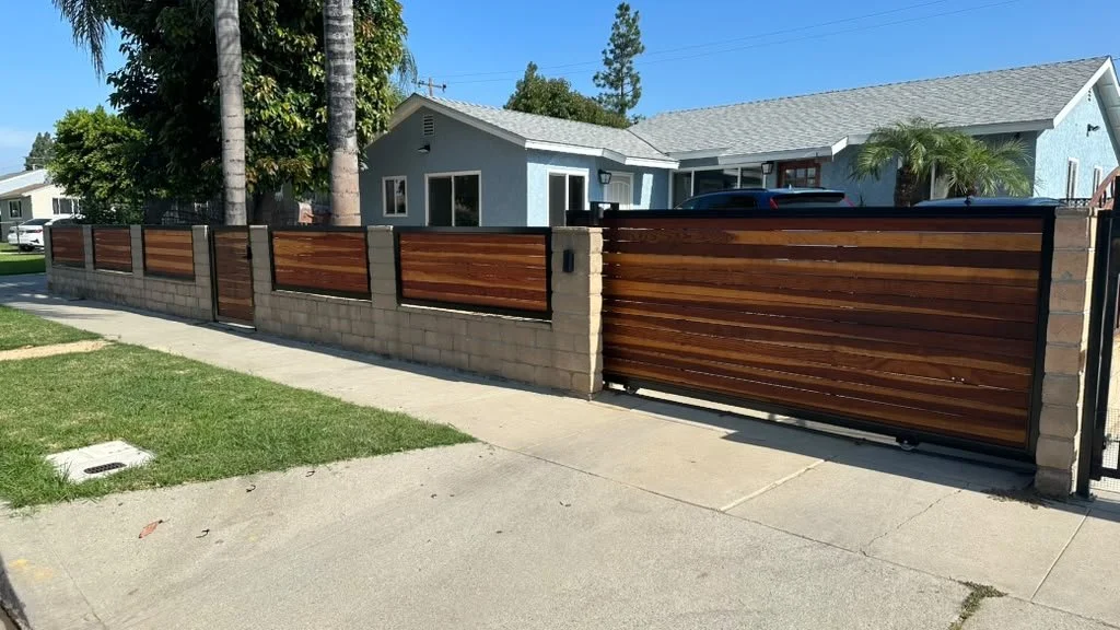 Residential house with a wooden and brick fence, sidewalk, and grass in front.