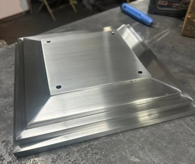 Metal step or platform with a beveled edge, placed on a workbench in a workshop setting.
