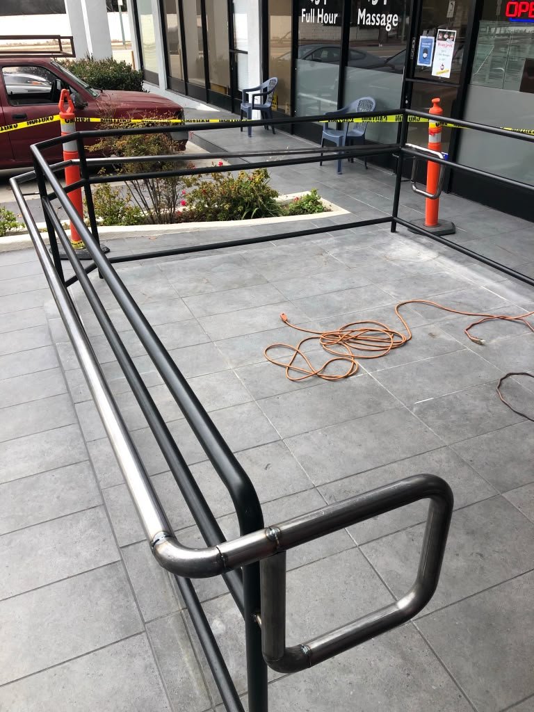 A wheelchair ramp outside a building, surrounded by orange cones and caution tape, with a coiled extension cord on the ground.