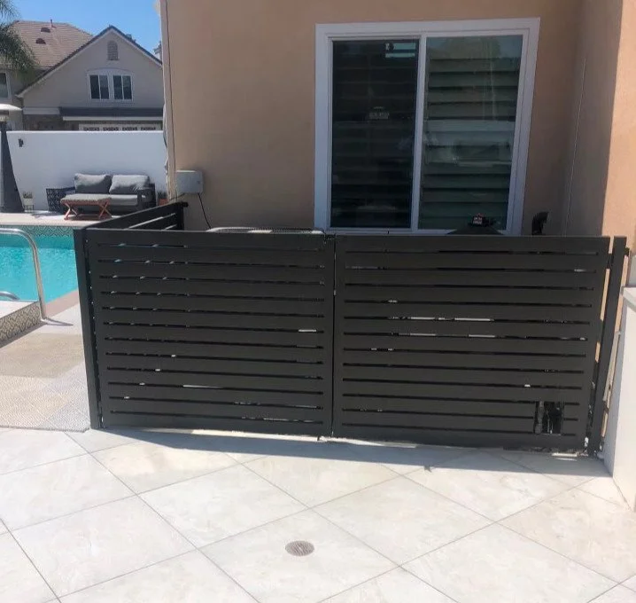 A black metal privacy gate in front of a sliding glass door, with a backyard pool and patio furniture in the background.
