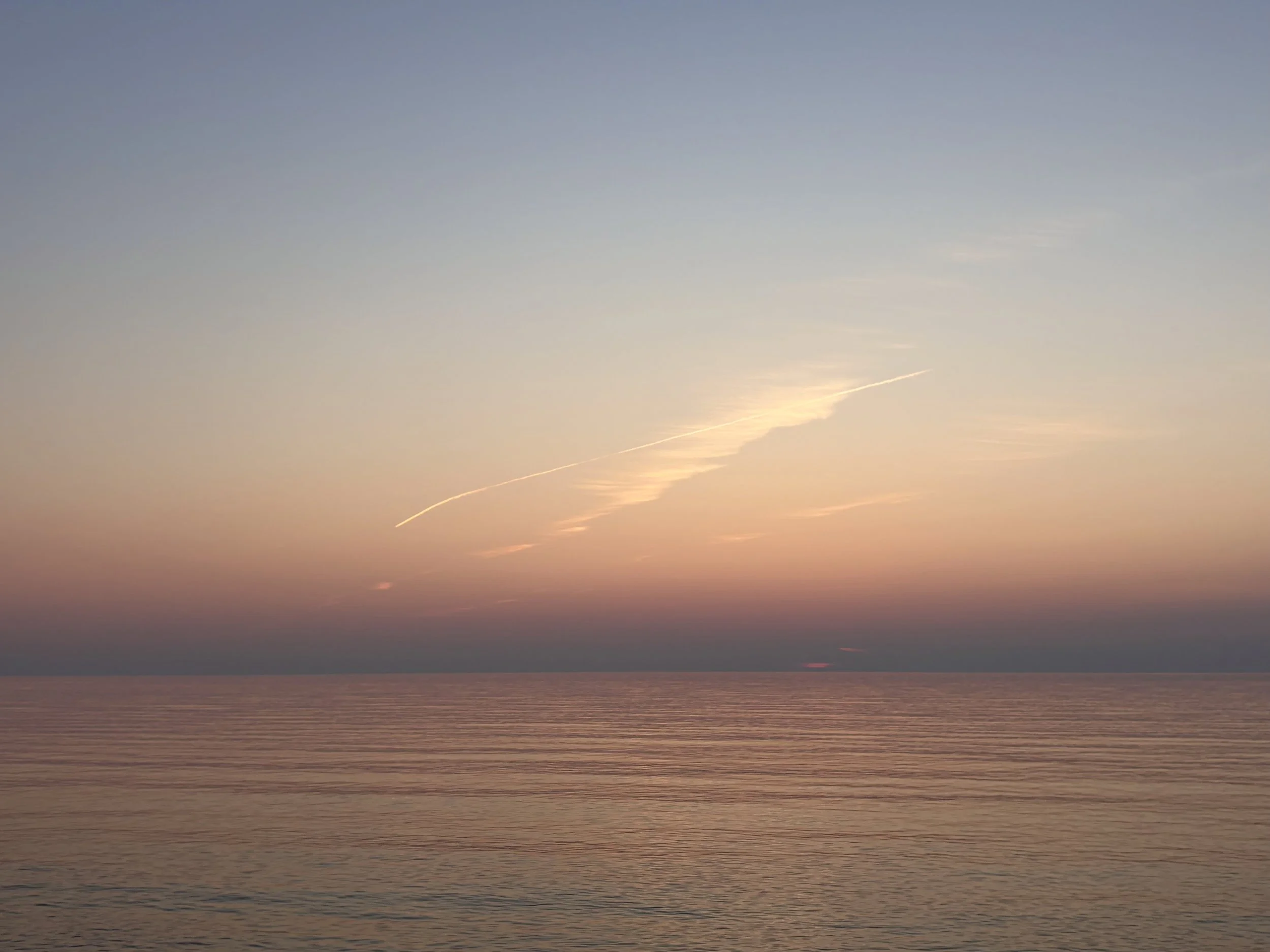 A sunset over the ocean with a clear sky and some high-altitude clouds.