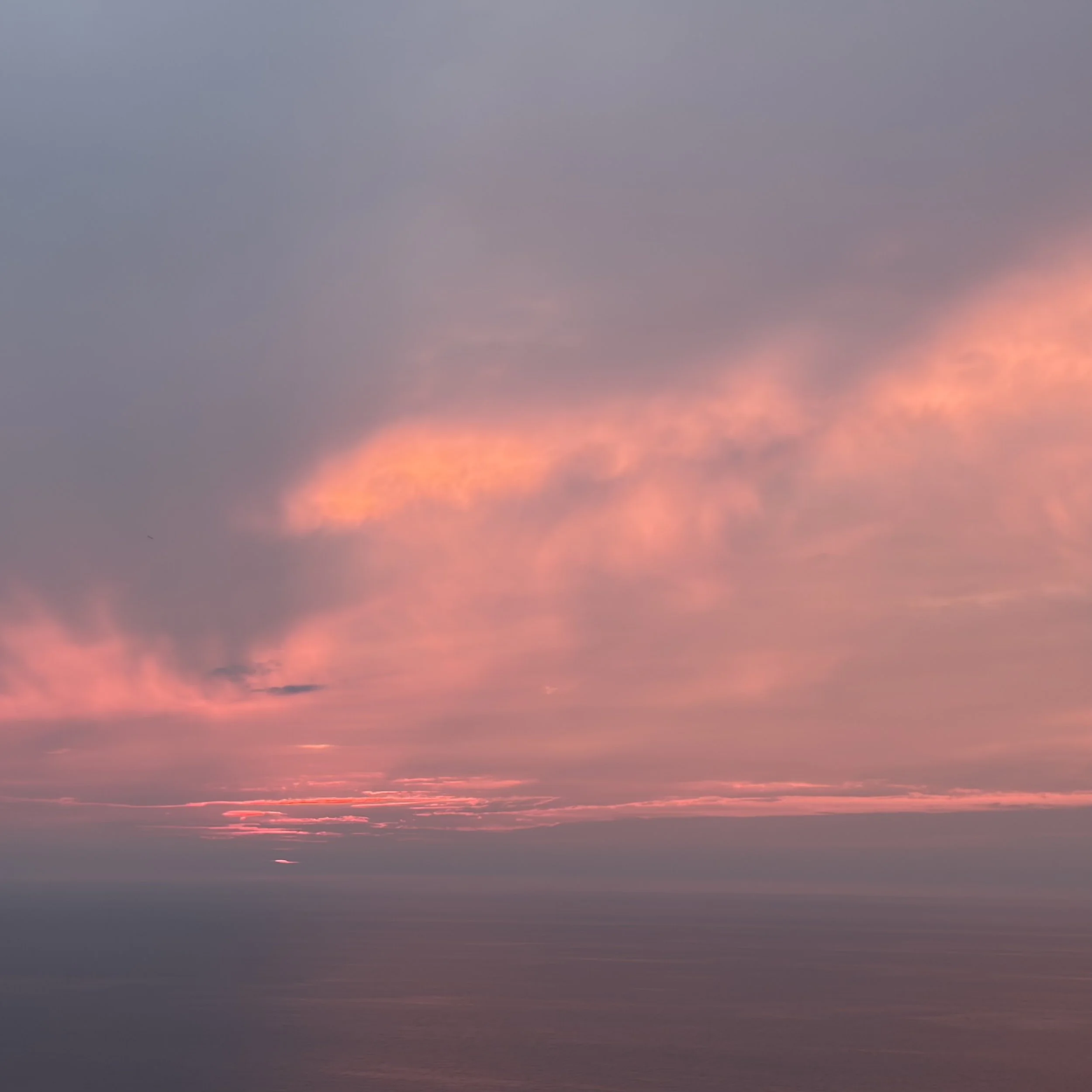 A sunset over the ocean with pink and purple clouds in the sky.