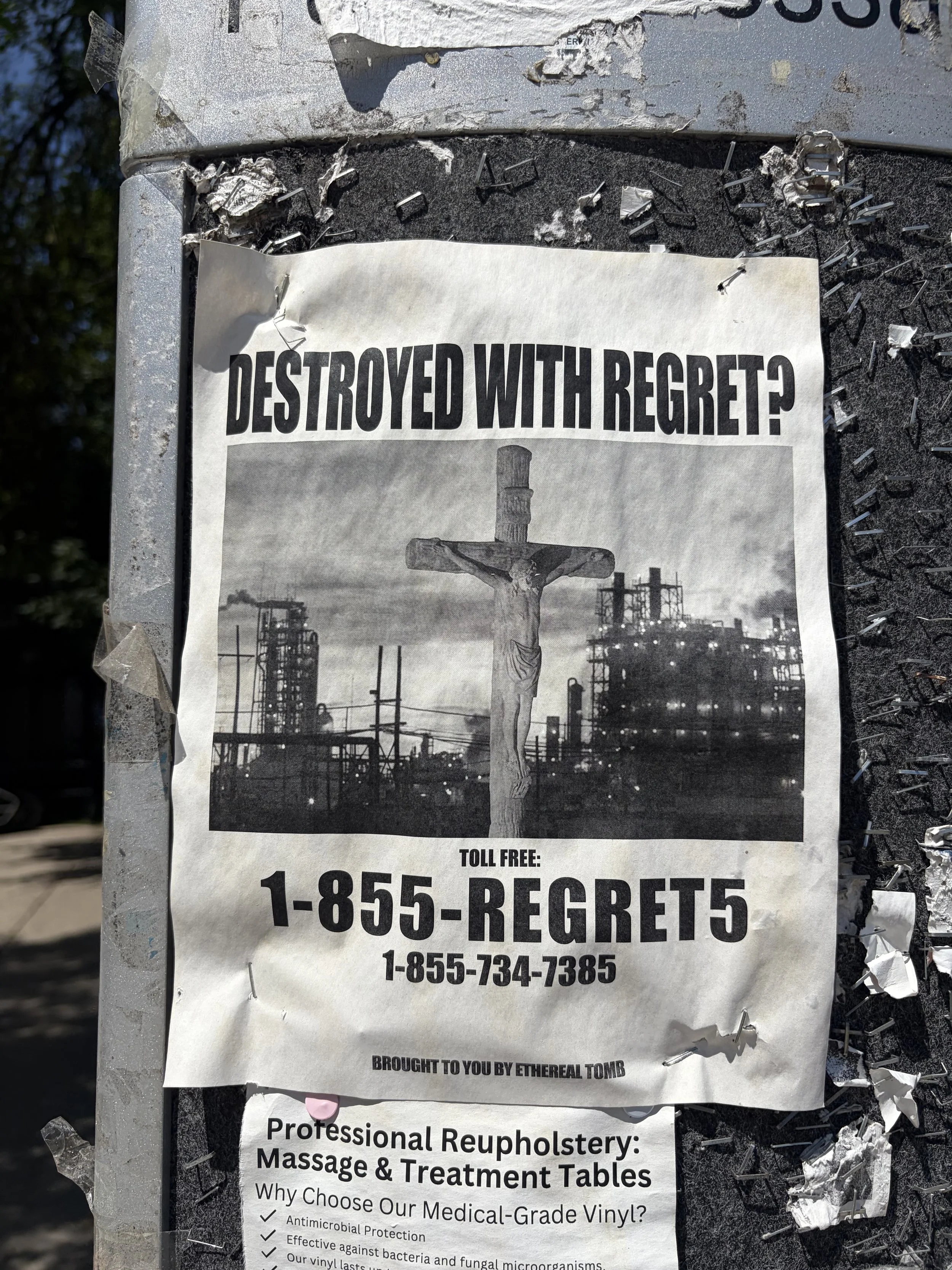 A damaged metal surface with a black and white poster advertising a memorial for Regret. The poster features a crucifix and industrial background. Text includes a toll-free number 1-855-REGRET5 and a statement about the memorial. The poster appears torn and weathered.