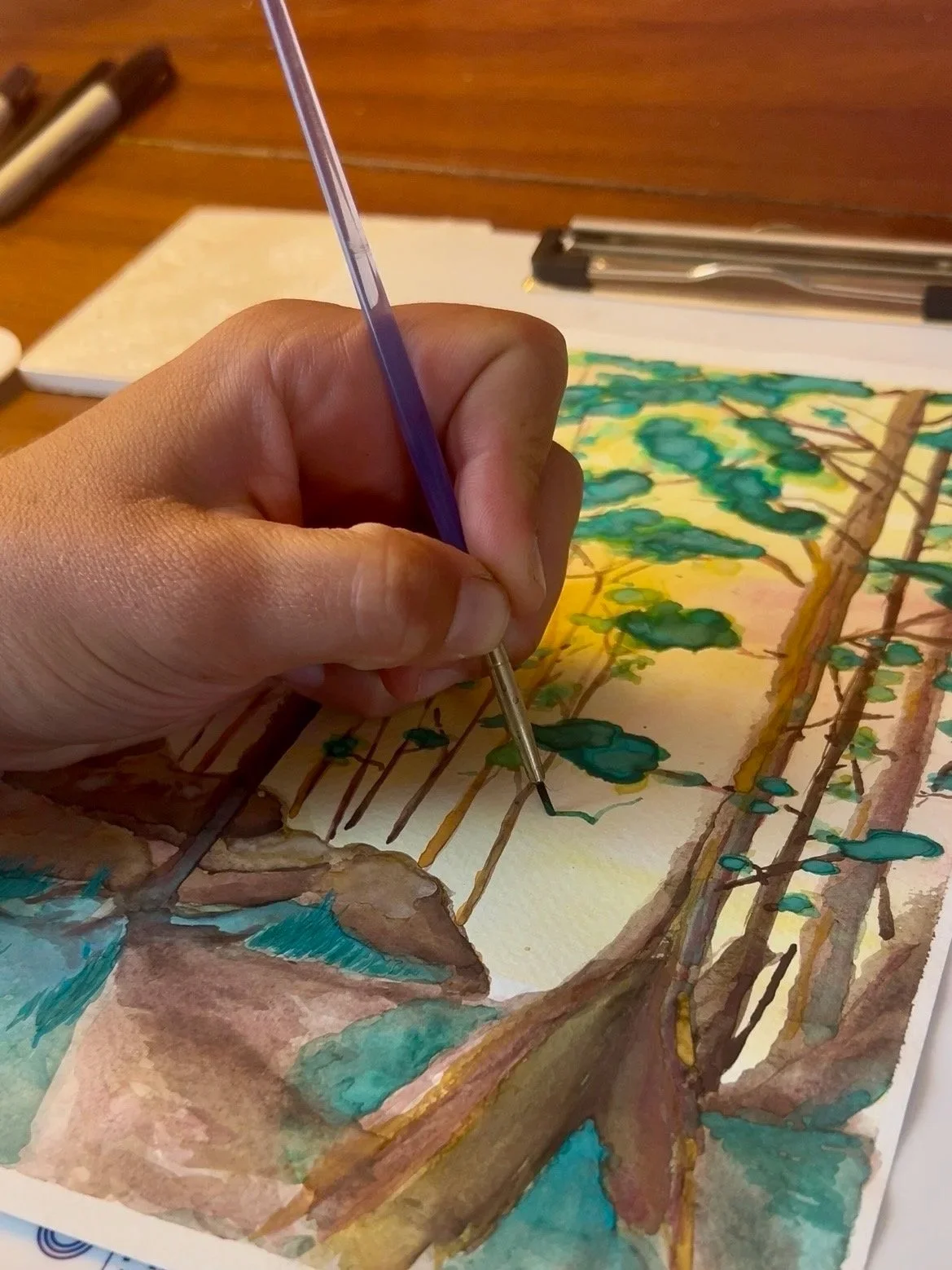 A person painting a watercolor of a tree with green leaves and brown branches.