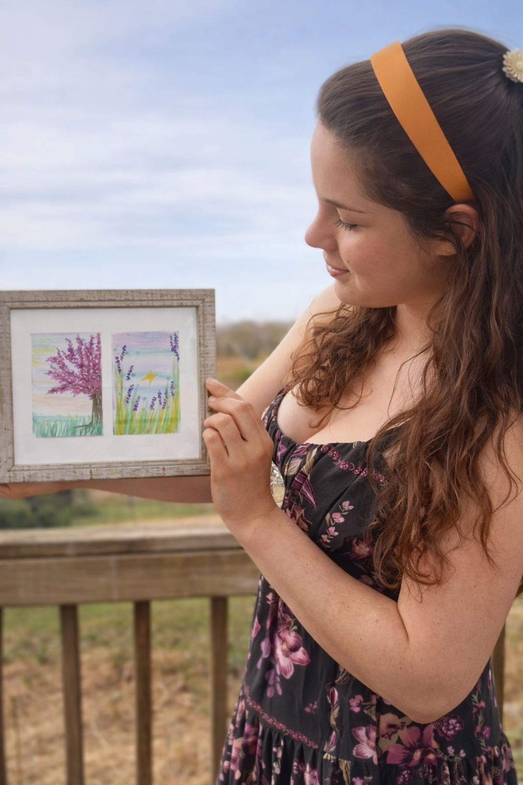 Color artist Abigail Lynn holding a small frame with two watercolors in it: - One of a tree with purple leaves - The other of a meadow with a yellow butterfly