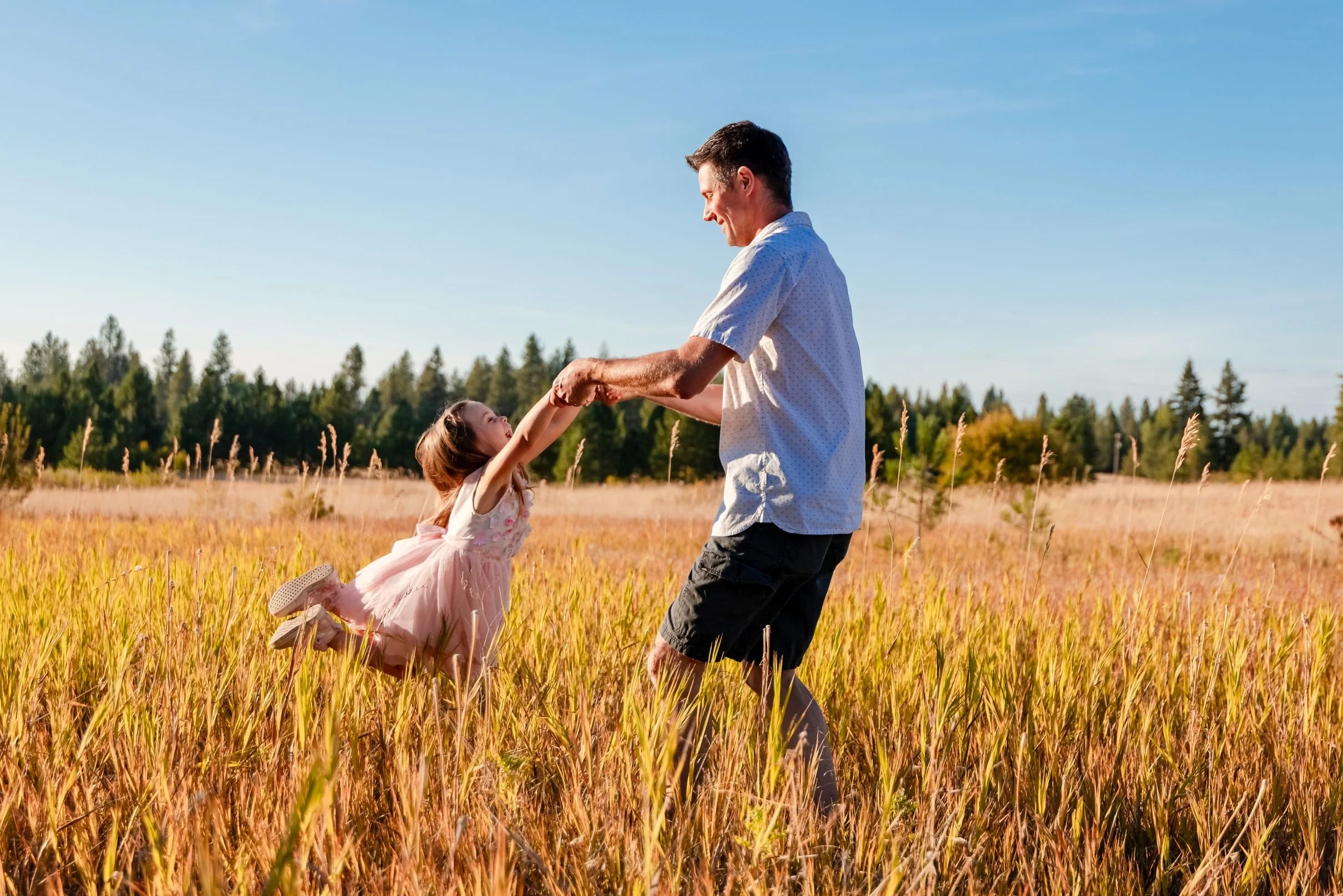 father swinging daughter in meadow during family photo session