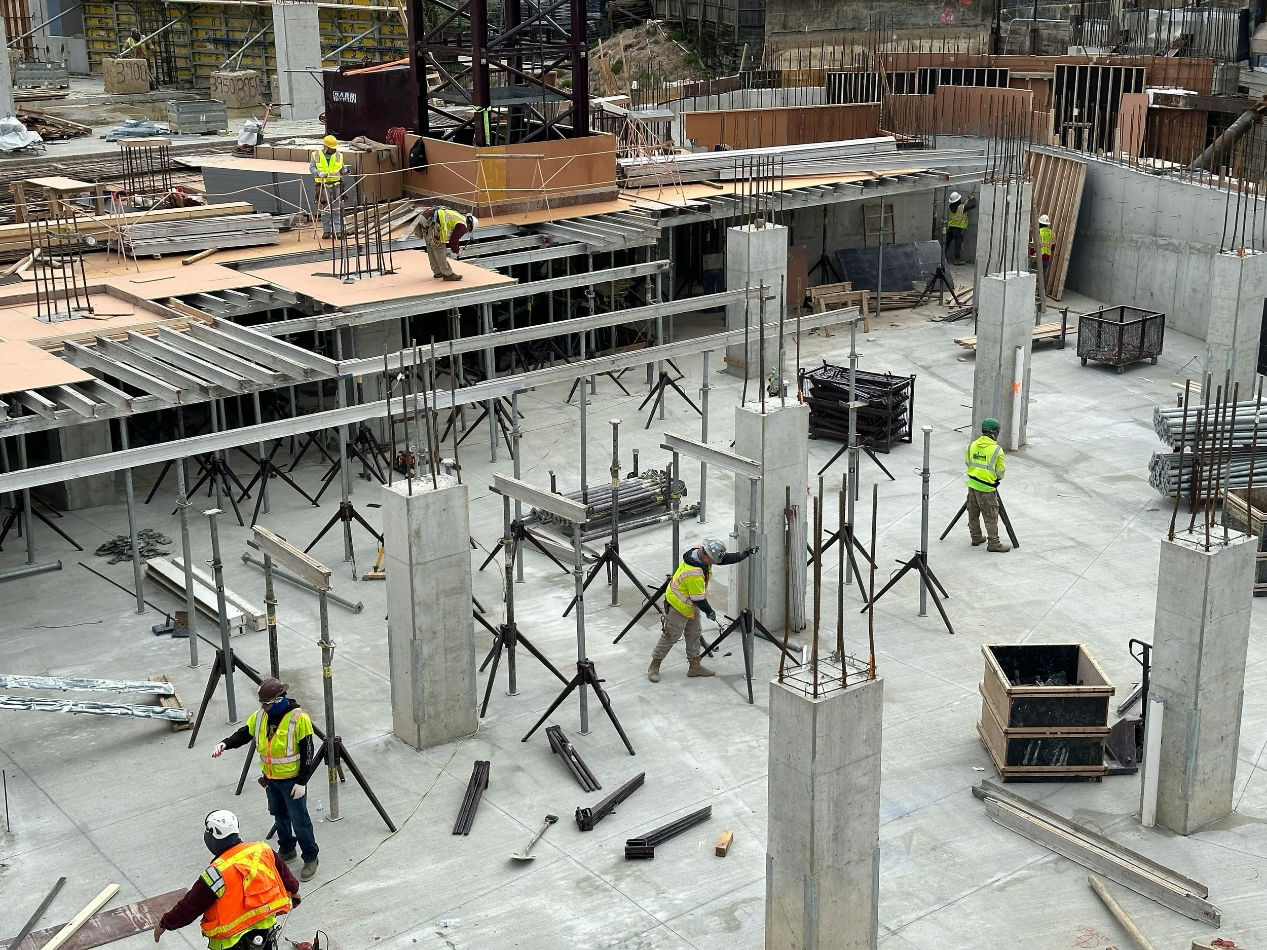 Construction workers on site with steel framework, plywood, concrete, and construction materials for building a structure.