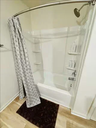 Bathroom shower with a curved shower curtain rod, partially open patterned shower curtain, and white tiled walls with built-in shelves.