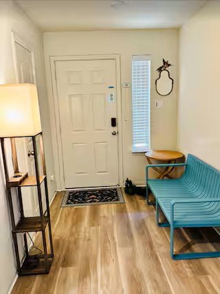 Entryway with a white door, a narrow window, a blue bench, and a wooden chair with a backrest, next to a small table with a lamp.