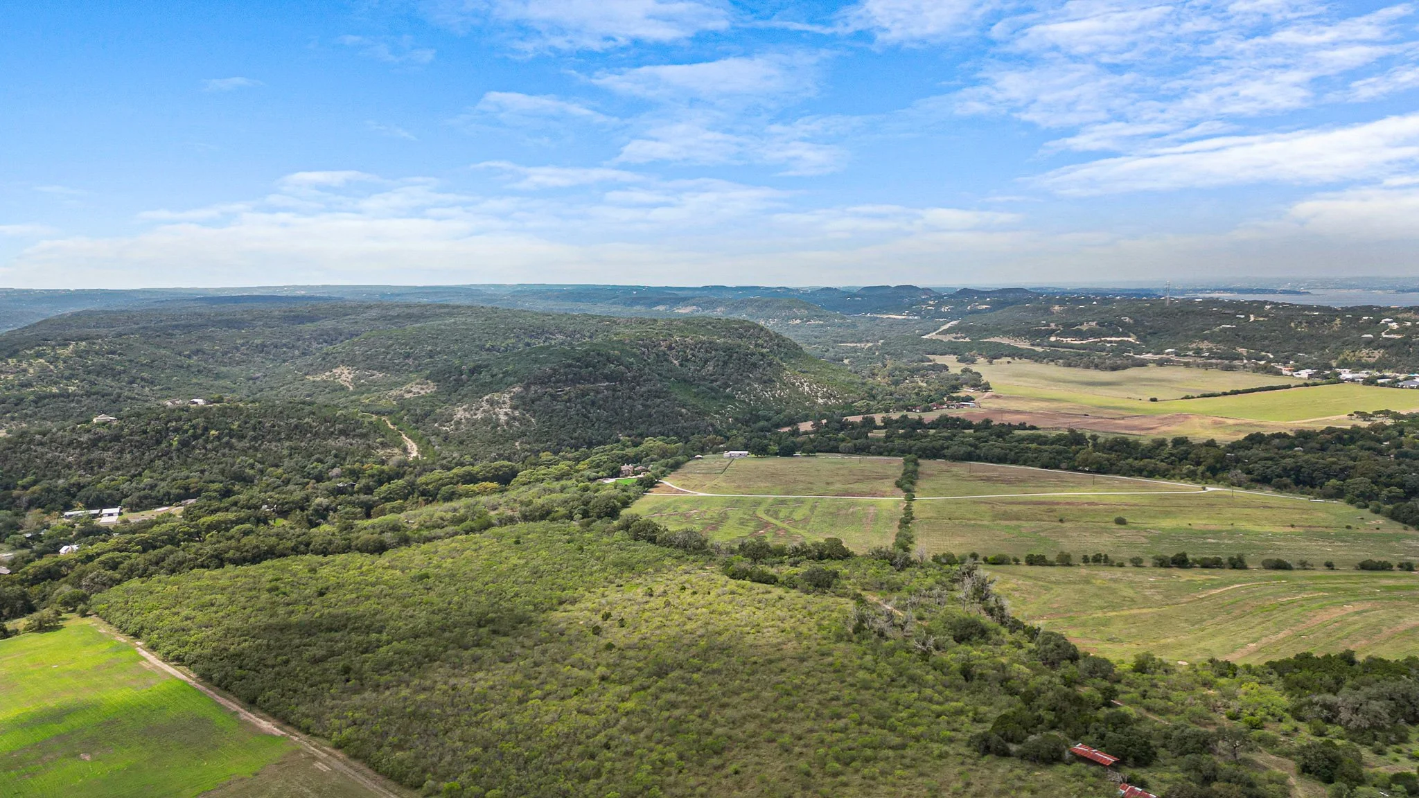Aerial view of rolling green hills, patches of farmland, and a blue sky with scattered clouds.