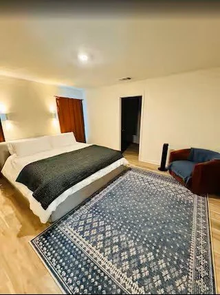 Bedroom with bed, blue armchair, rug, and doorway.