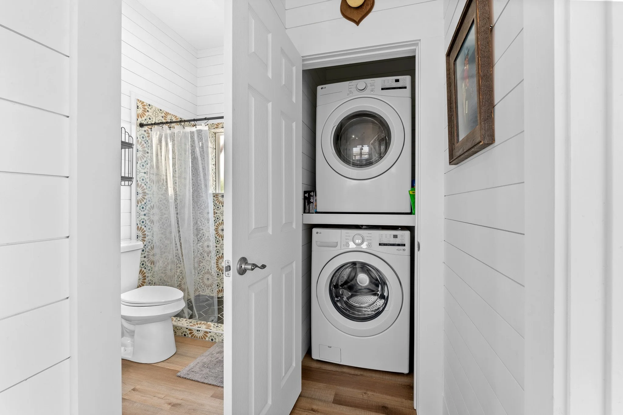 Laundromat closet with stacked washing machine and dryer, view from doorway, adjacent bathroom with toilet and shower curtain