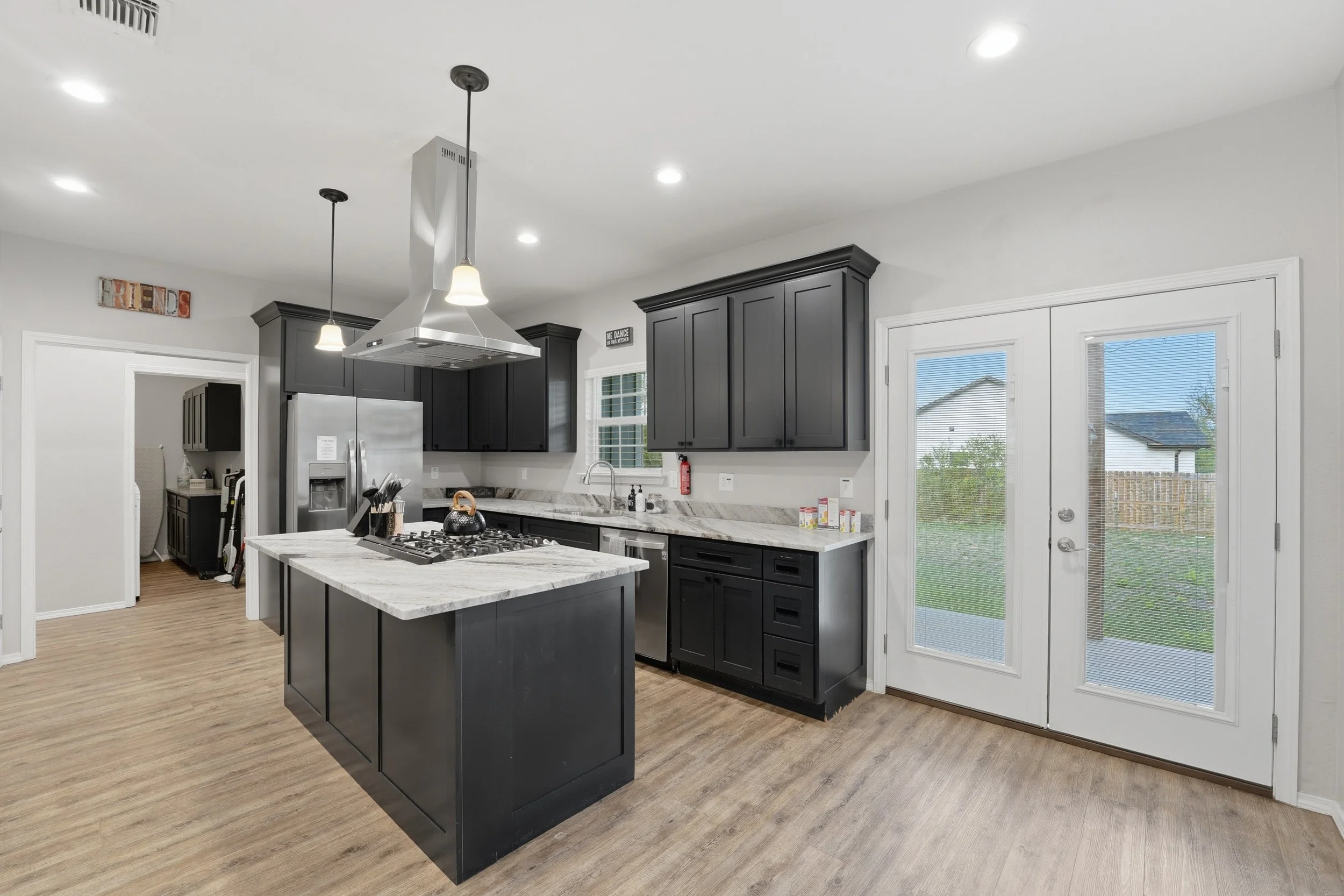 Kitchen with black cabinets, a central island with a marble top, stainless steel appliances, and a sliding glass door leading outside.