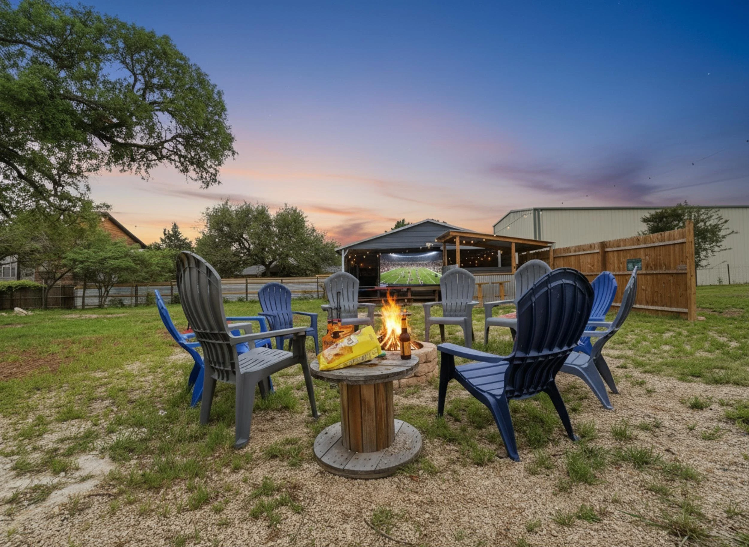 An outdoor backyard scene during dusk with a fire pit surrounded by chairs, a barbecue grill, and a view of a football stadium in the distance under a sky with pink and purple hues.