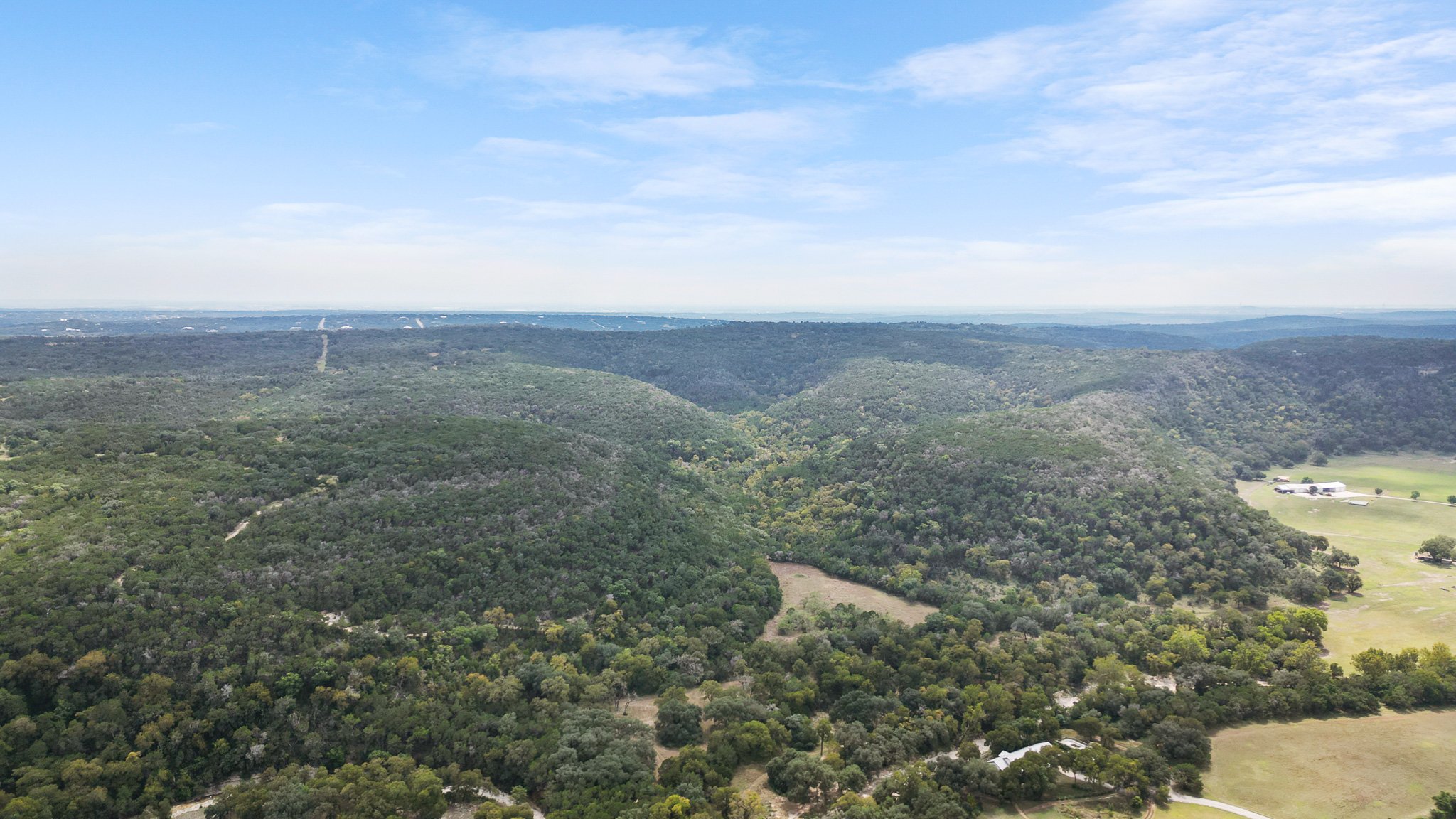 Aerial view of a large forested valley with rolling green hills under a partly cloudy blue sky.