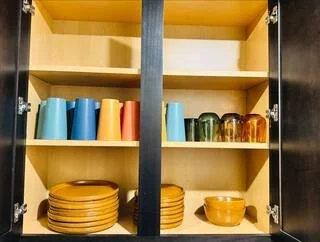 Open kitchen cabinet with colorful cups and stacked plates inside
