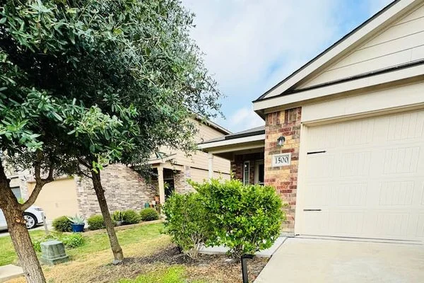 Front yard of a suburban house with a brick exterior, garage, bushes, and a tree.