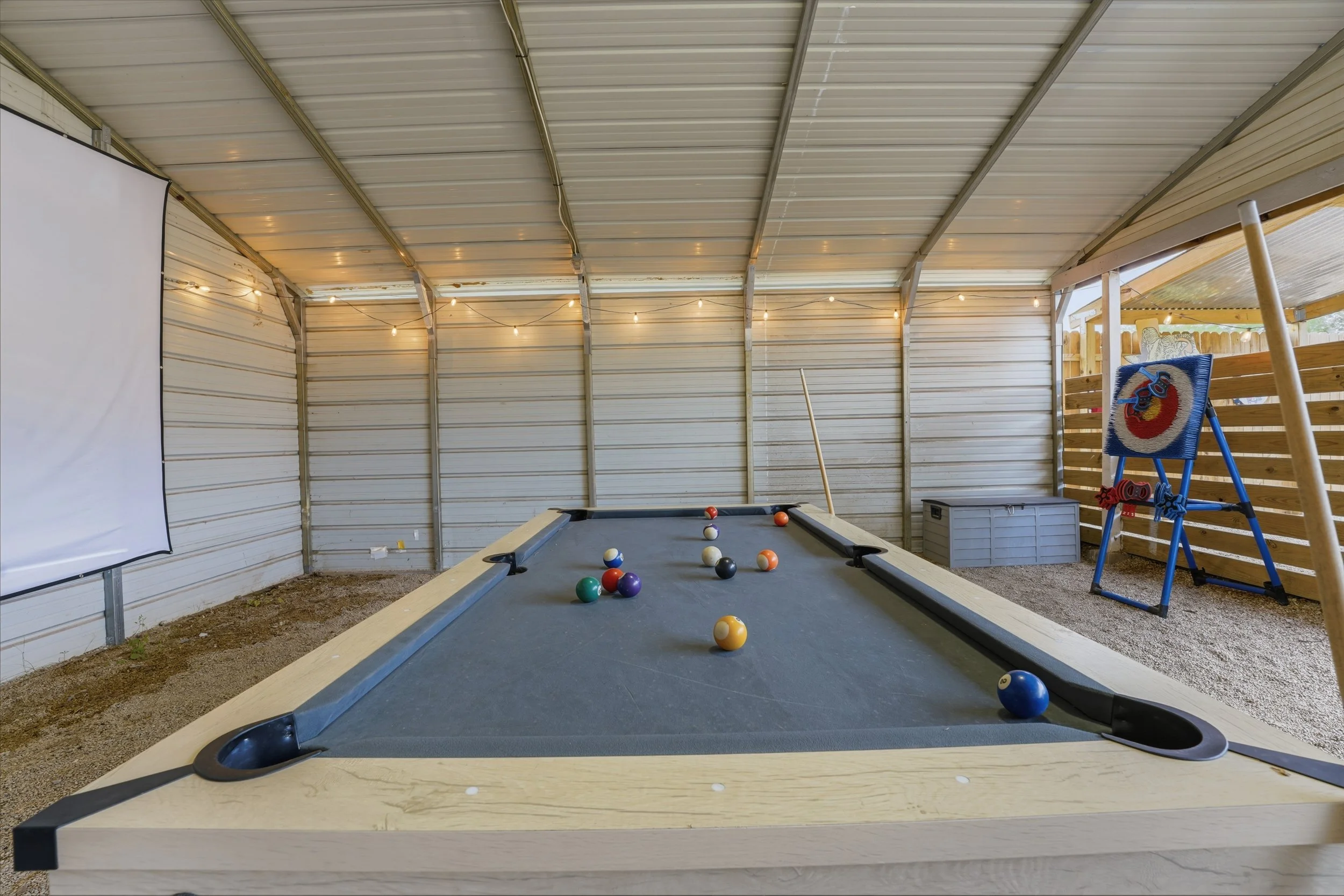 Indoor shed with string lights, a pool table with billiard balls, a lounge chair, and a small TV on a wooden railing.