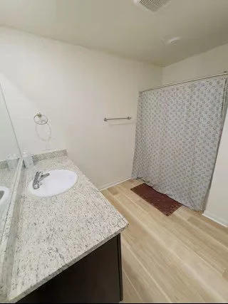 Bathroom with granite countertop, sink, mirror, towel rack, shower curtain, and wooden floor.