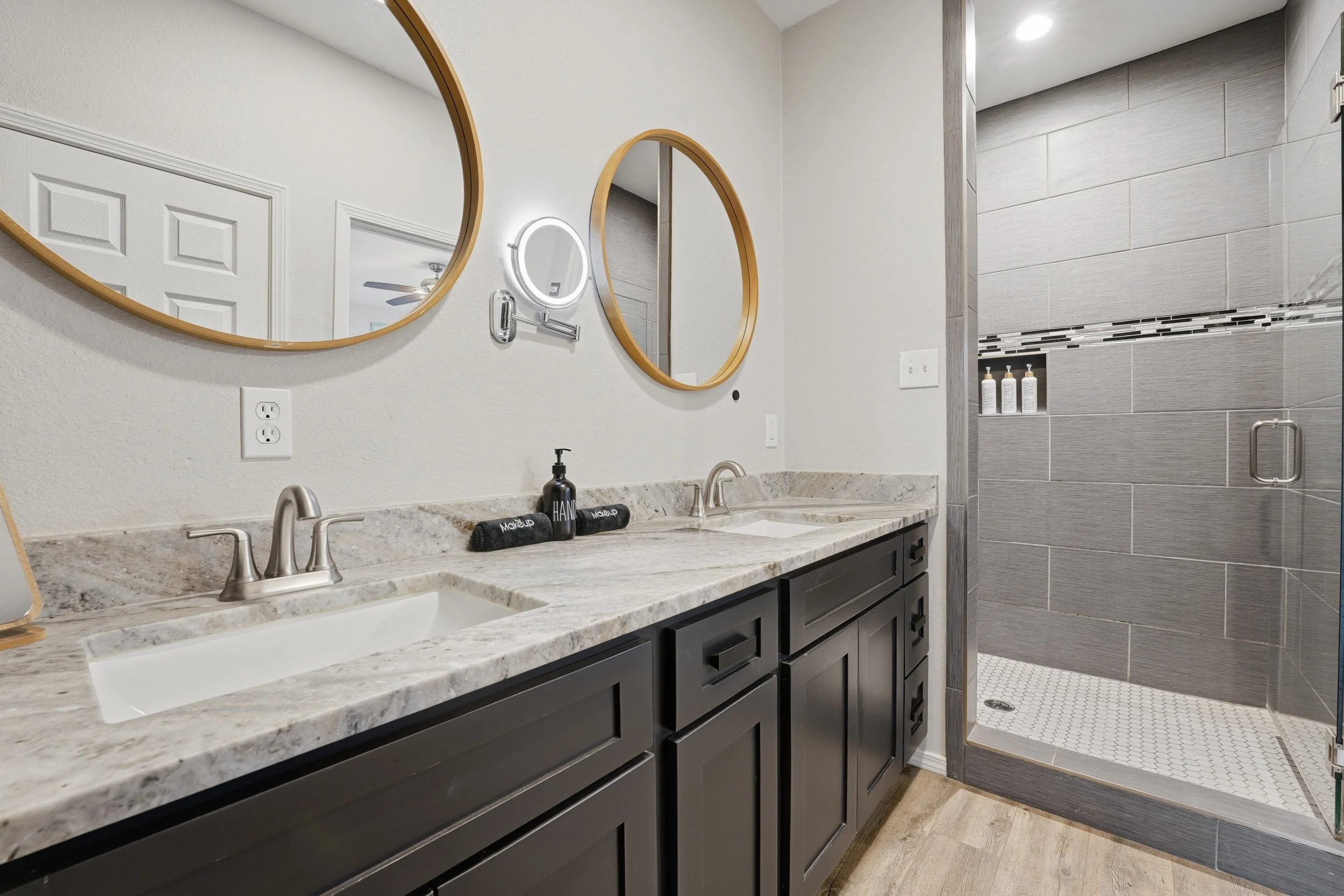Modern bathroom with double sink vanity, round mirrors, and a shower with gray tile walls.