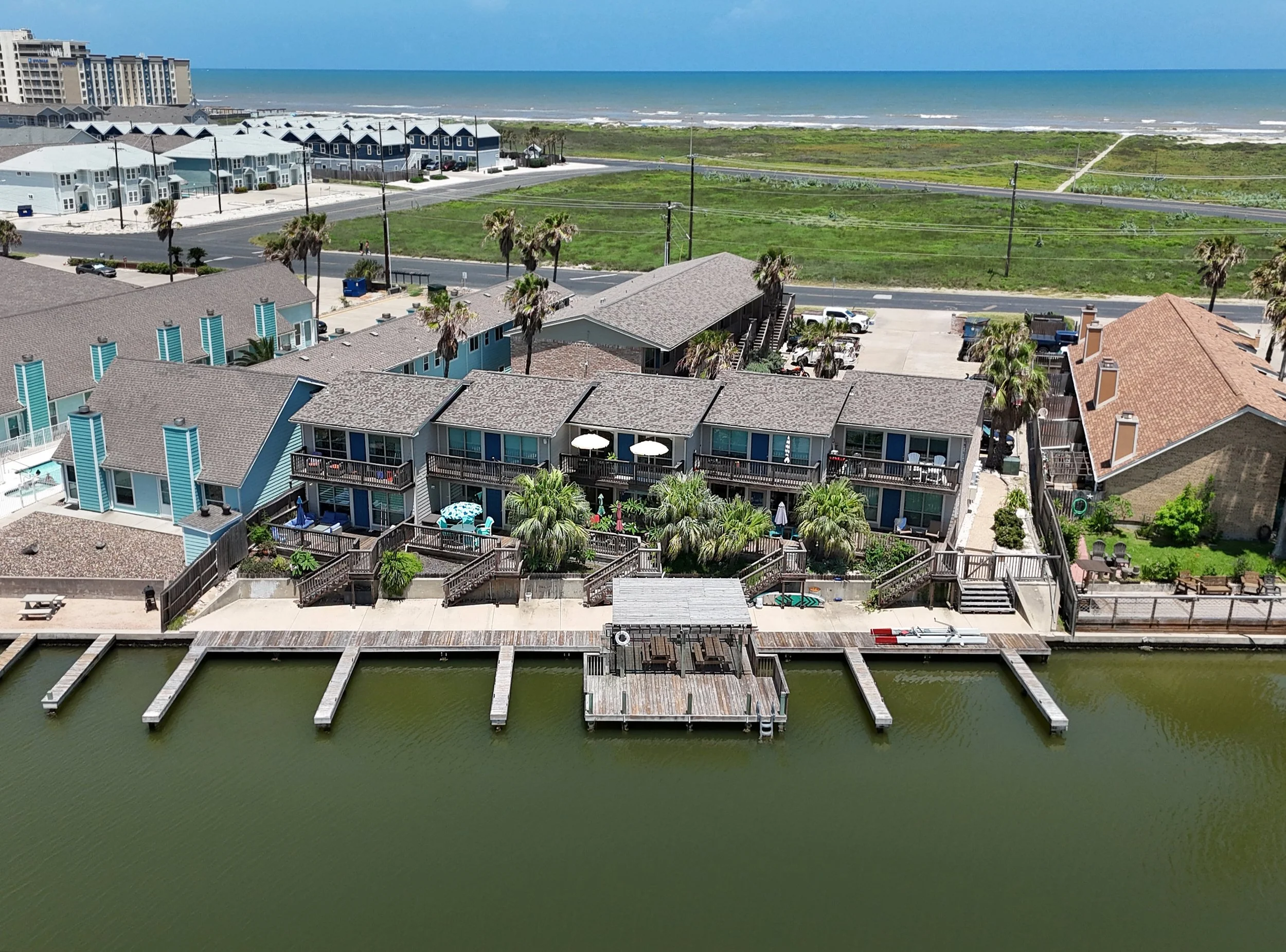 Aerial view of beach houses along a canal with a sandy beach and ocean in the background.