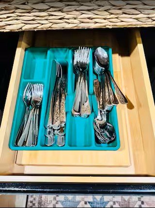 Organized kitchen drawer with silverware, including forks, knives, and spoons, inside a blue utensil tray.