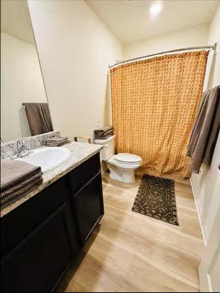 Bathroom with a granite vanity, mirror, toilet, shower with curtain, and towels.