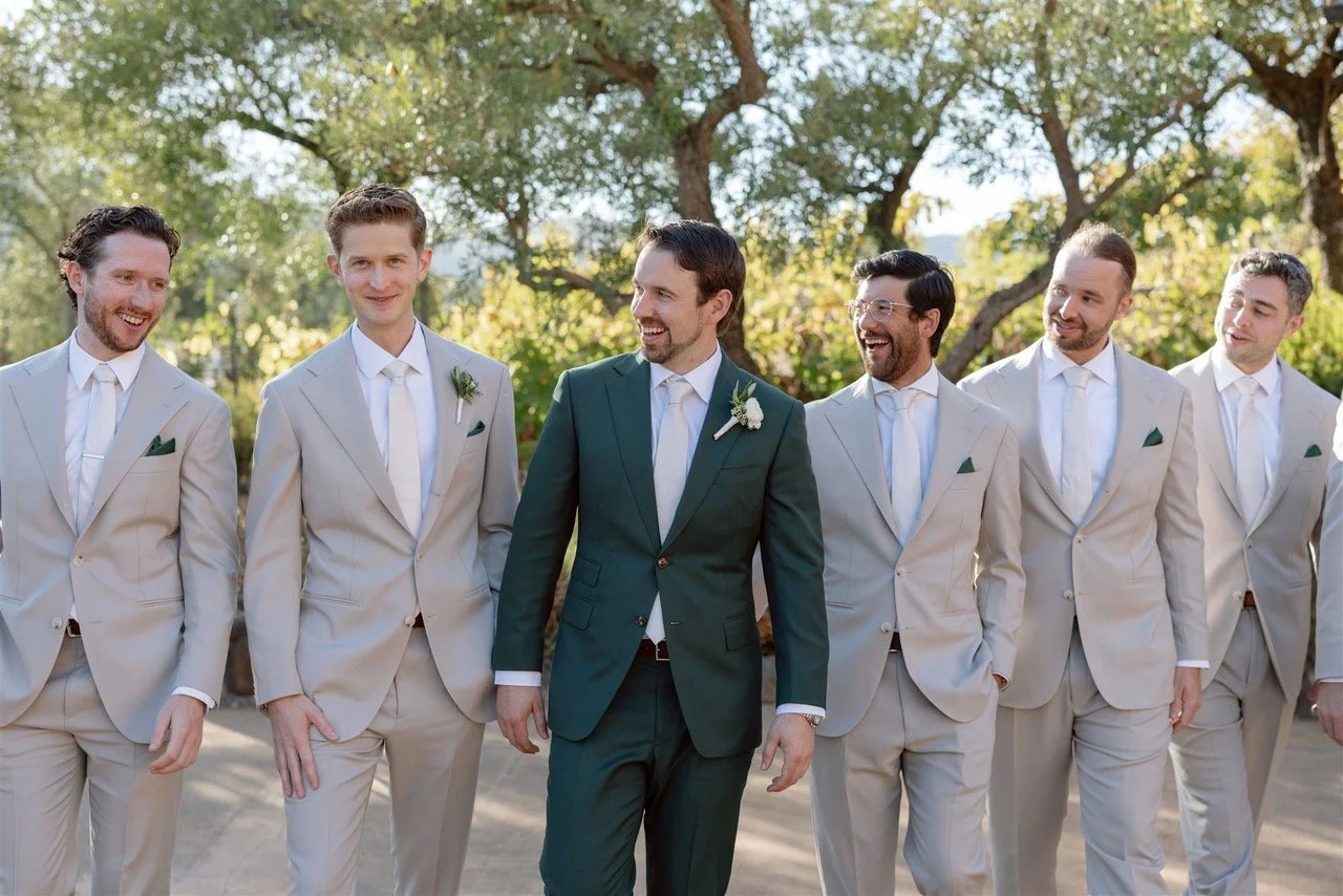 Group of men, the groom and wedding party in Scarborough Custom Tailoring suits walking outdoors on a sunny day, with trees in the background, celebrating a wedding.
