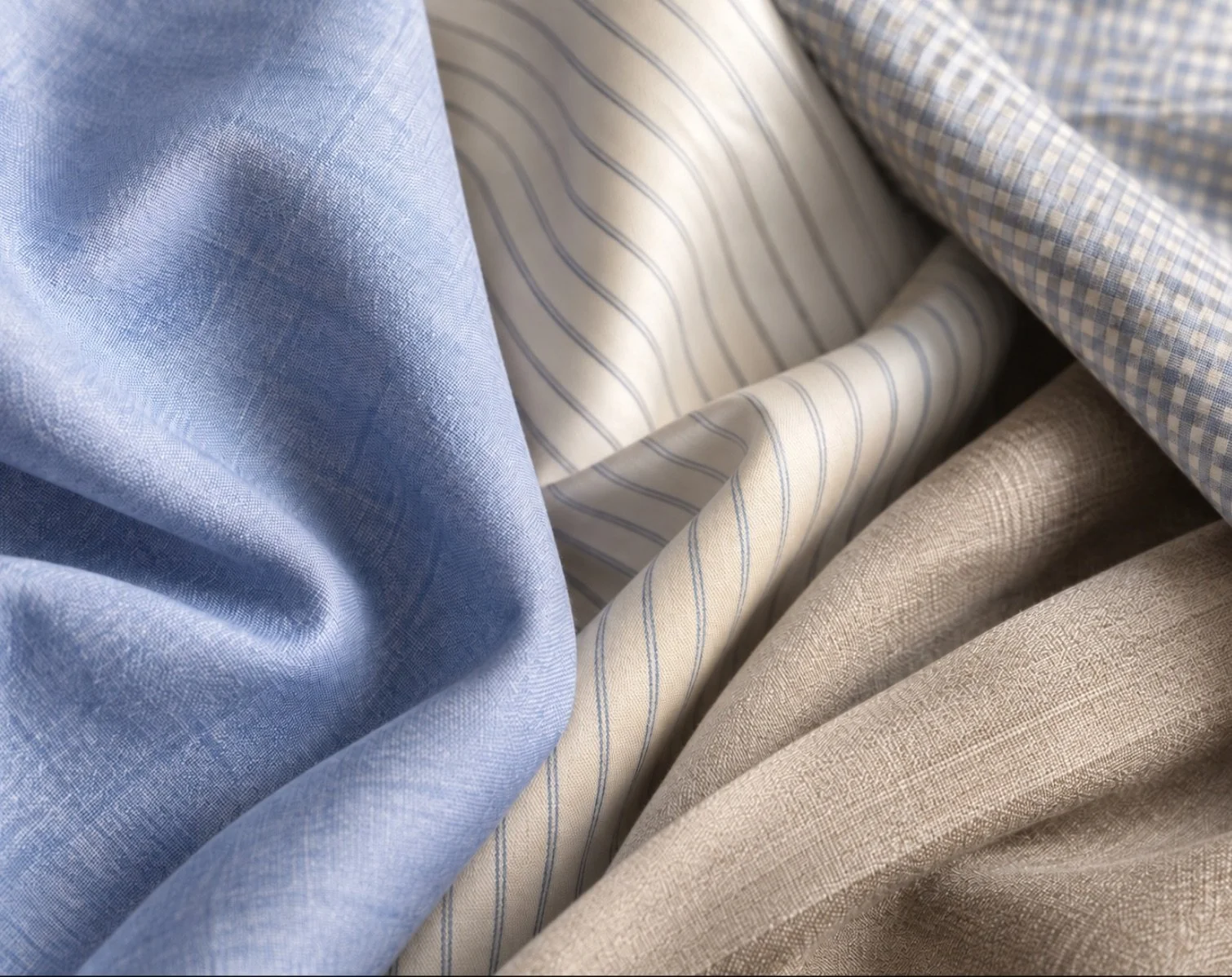 Shirting fabrics in light blue, cream with a blue pinstripe, blue gingham and taupe, draped together.