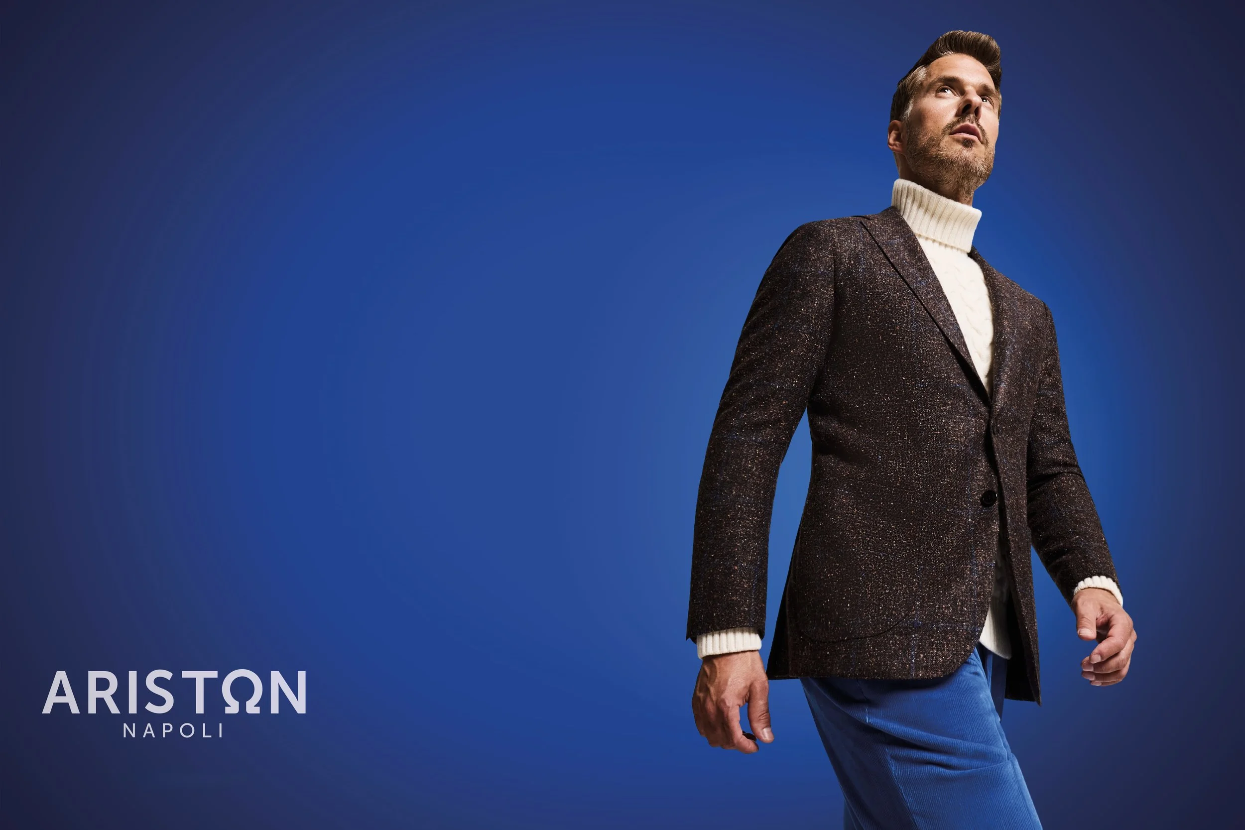 A man wearing a dark, sparkly blazer with a white turtleneck sweater underneath, standing against a blue background. The text on the image reads 'ARISTON NAPOLI'.