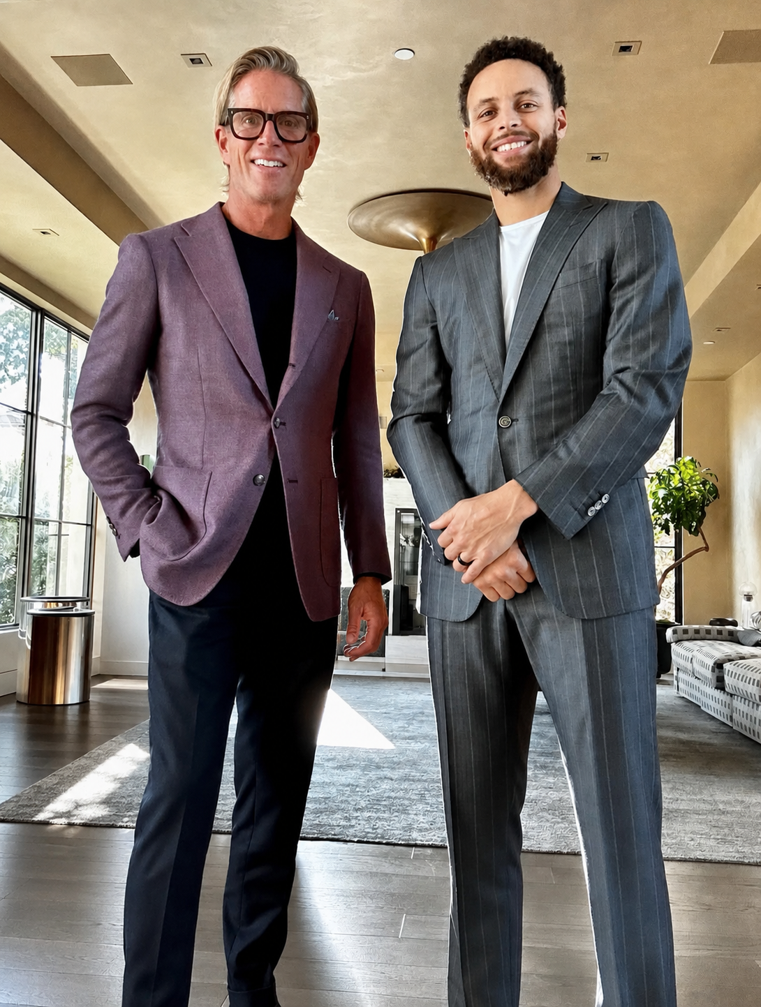 Christian Gardner and Stephen Curry in suits standing indoors in a well-lit room, smiling at the camera.