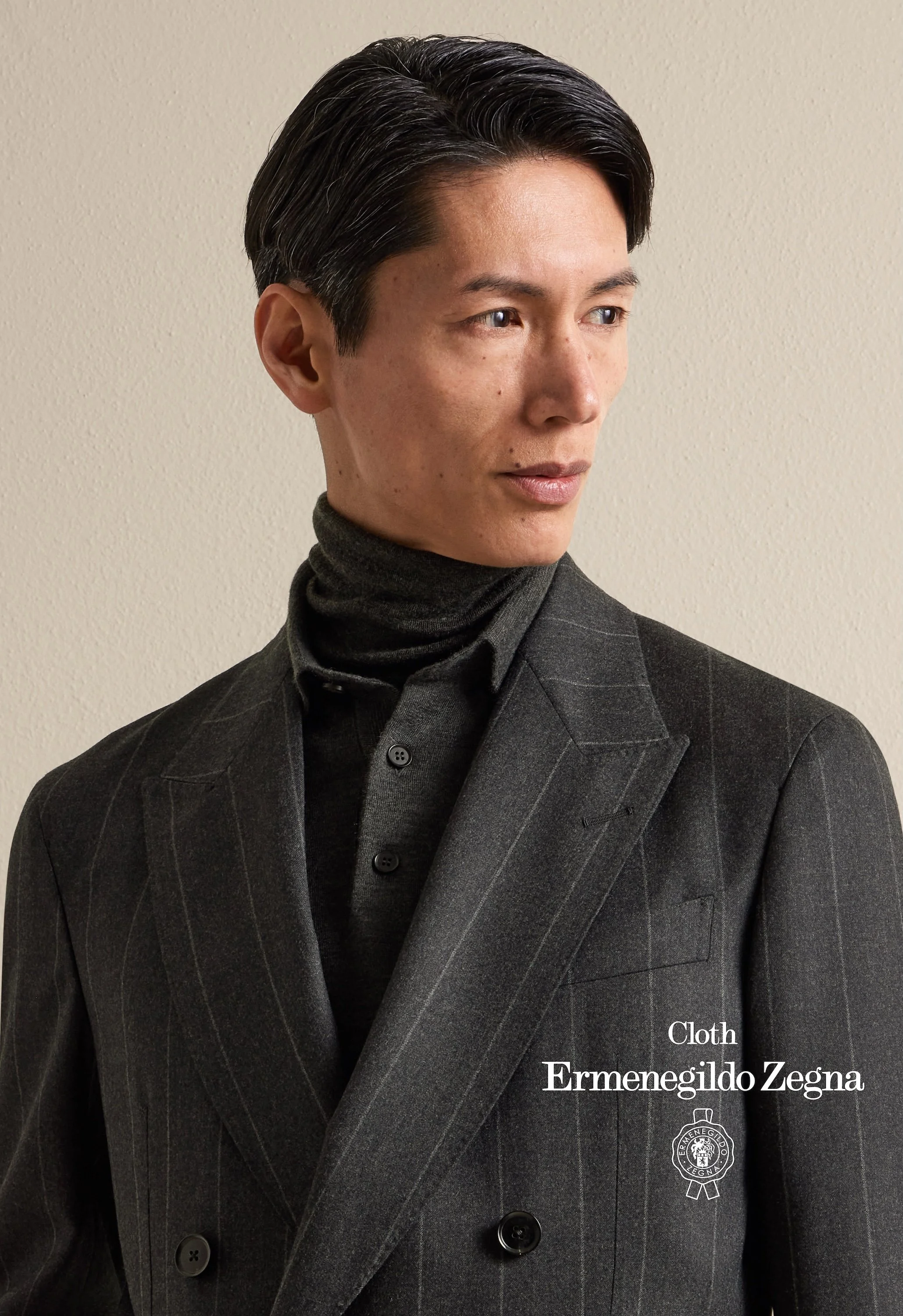 Close-up of a man wearing a black pinstripe suit and turtleneck sweater, with text overlay reading 'Cloth Ermenegildo Zegna' and the Zegna logo.