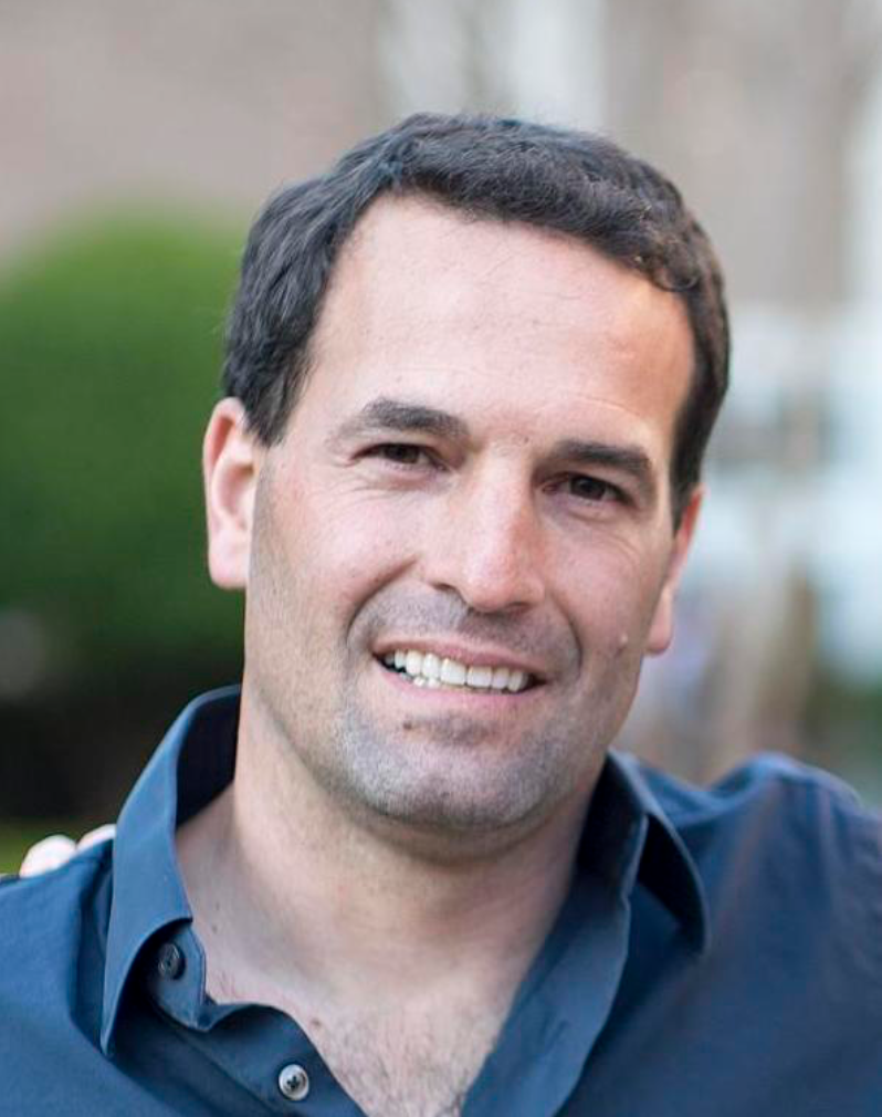 Close-up of a smiling man outdoors with blurred background.